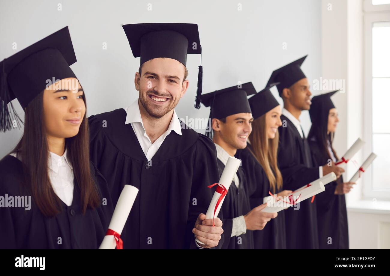 Student man with diploma in hands looking at camera standing next to his multiethnic classmates. Stock Photo