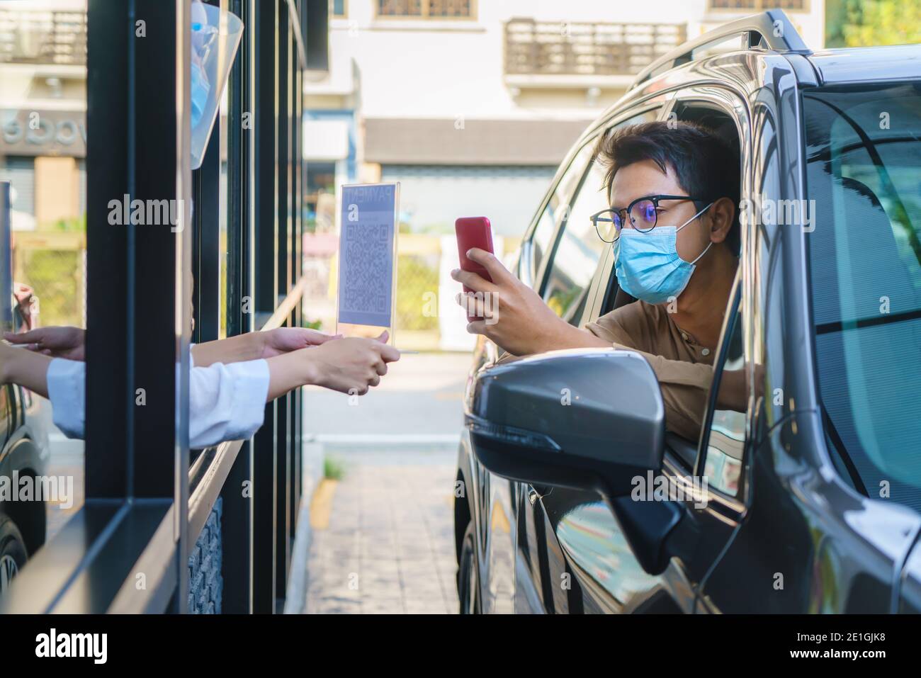Asian man customer using mobile scan QR or NFC payment on smart phone paying for his coffee drink in coffee shop while he drive thru and Barista weari Stock Photo