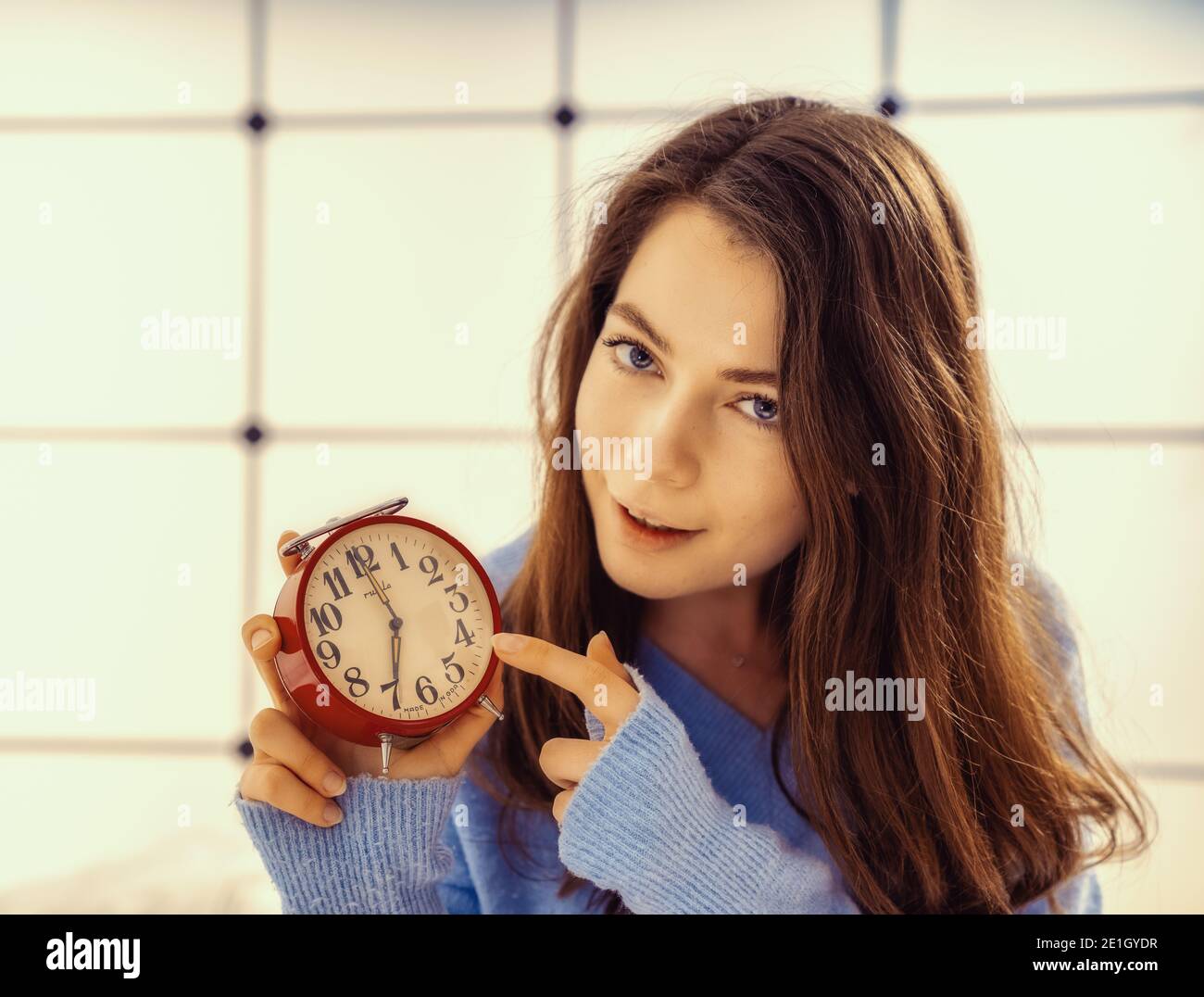 Beautiful young woman showing time on alarm clock Stock Photo Alamy