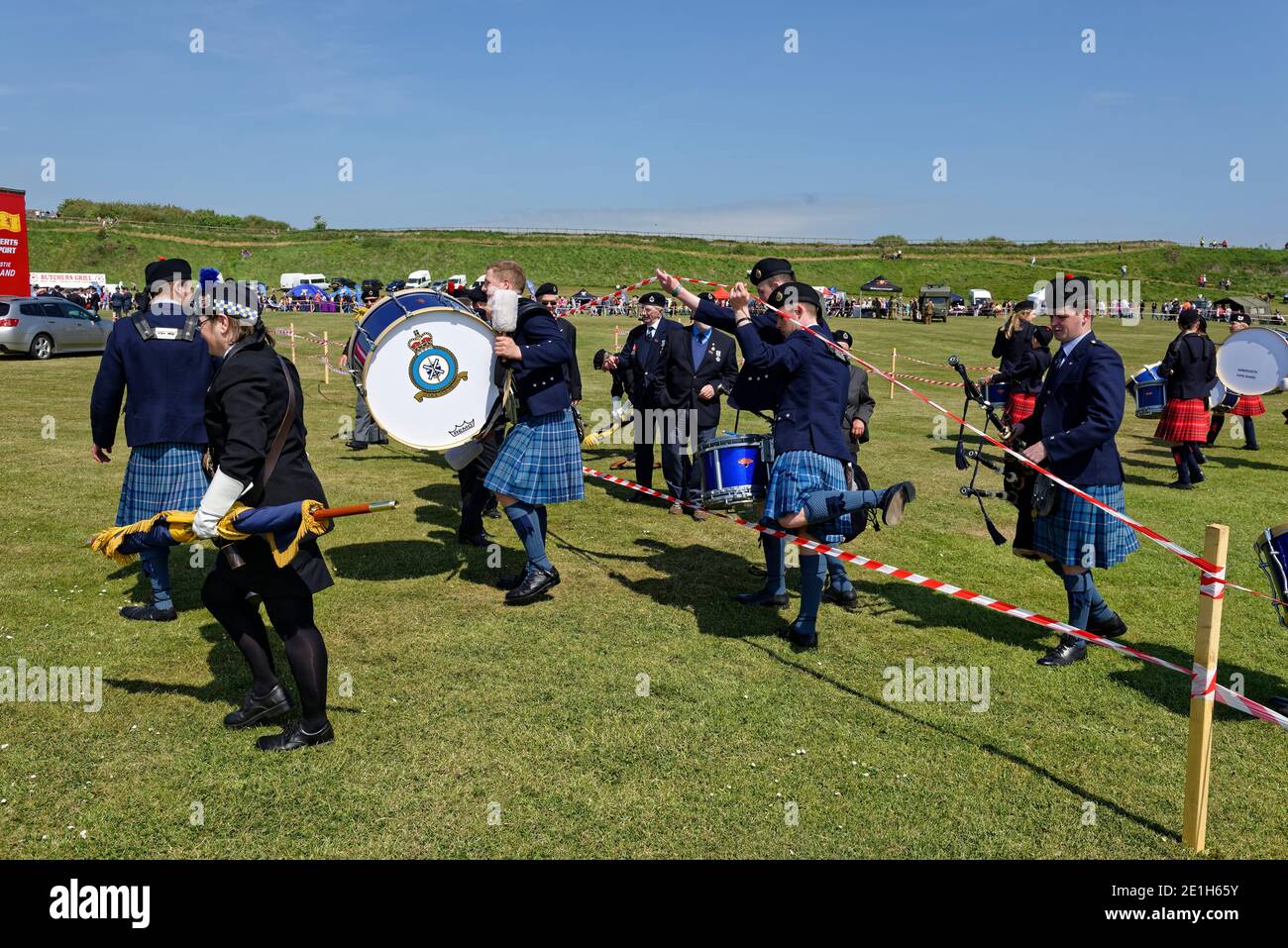 Members of a Marching Pipe band climbing over the temporary red and white tape barrier after their performance at an event in Arbroath. Stock Photo