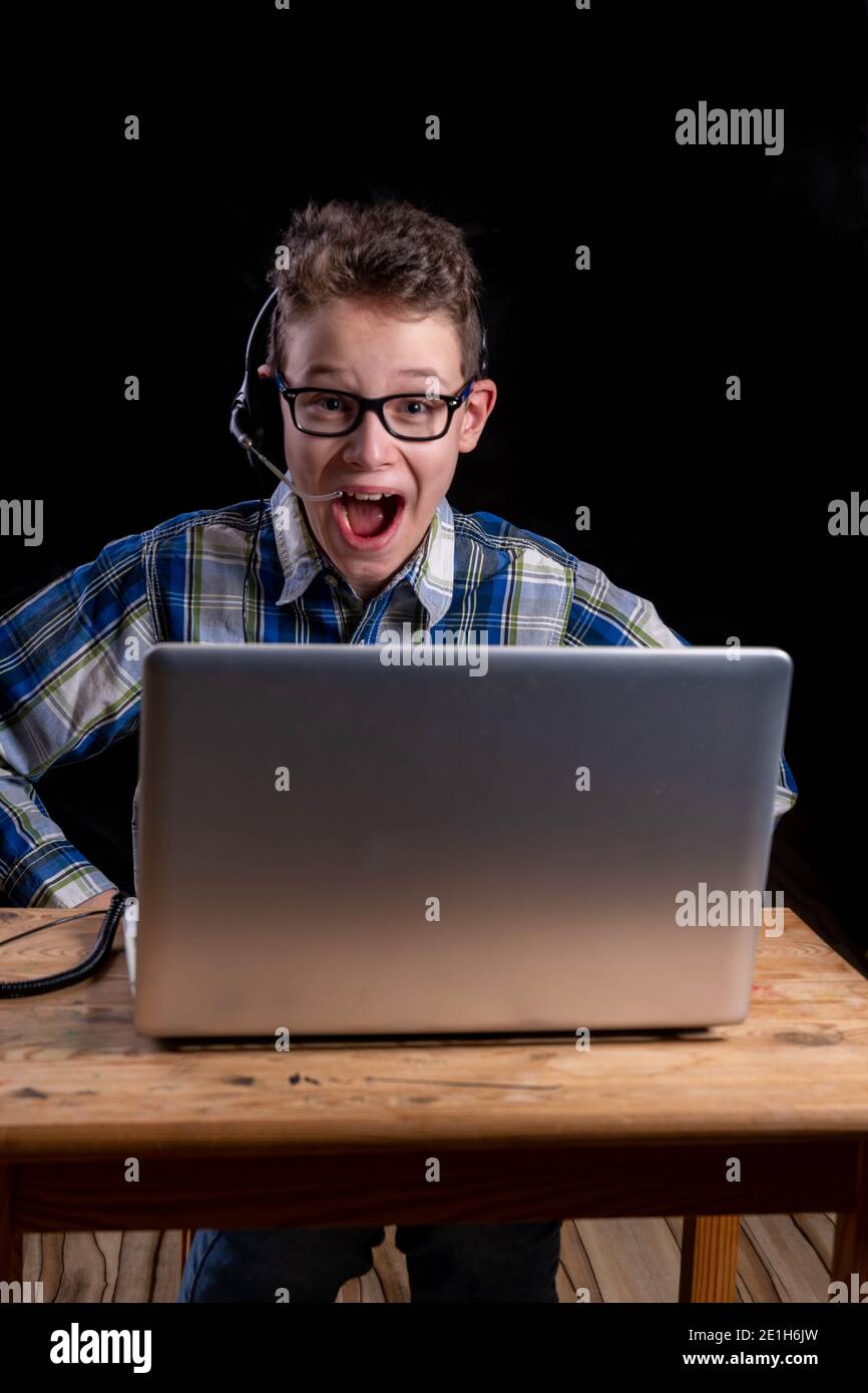 Boy with shirt and glasses joyfully using headset while e-learning on laptop Stock Photo
