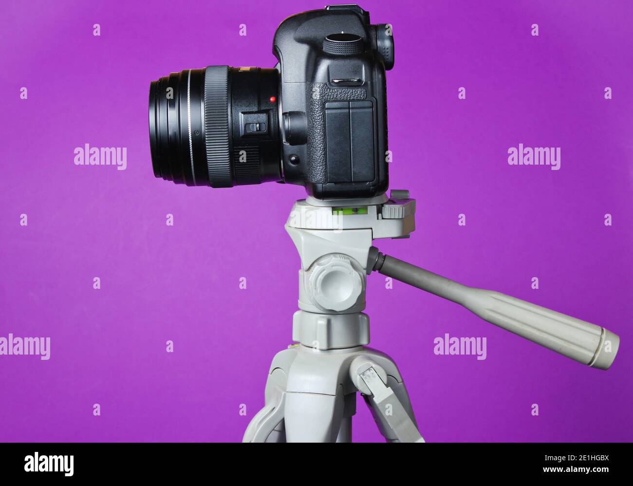 Modern digital camera with a tripod on purple background. Front view ...