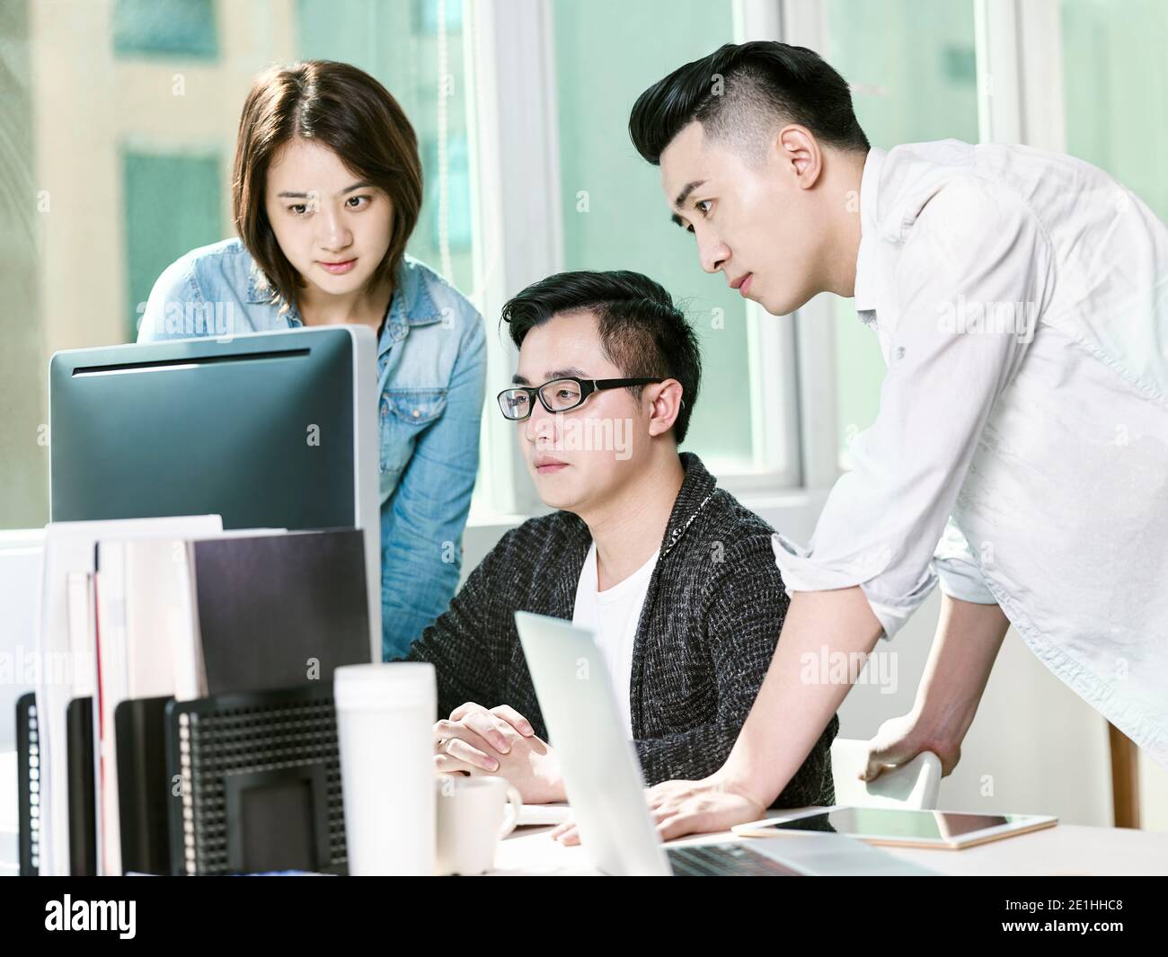 team of three young entrepreneurs analyzing data in office using desktop computer Stock Photo