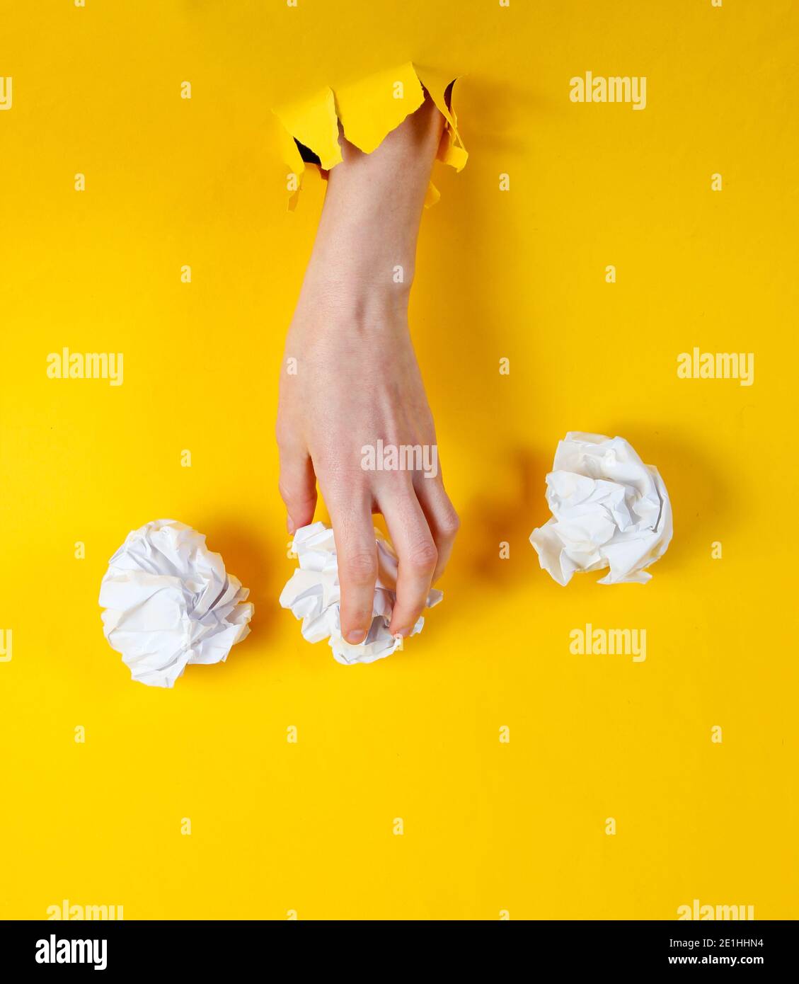 Female hand holds crumpled balls of paper through torn yellow paper
