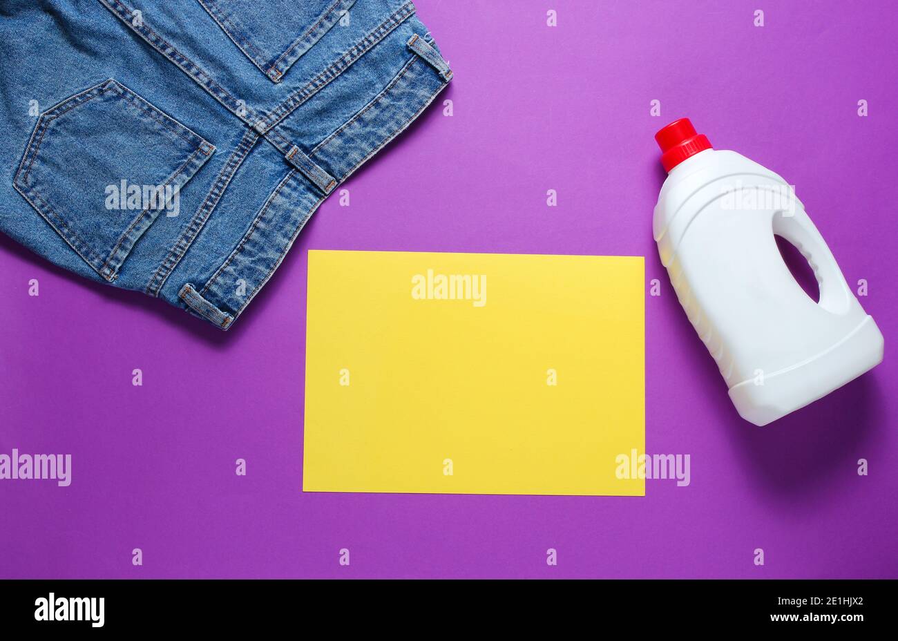 Minimalistic concept of washing. Paper for copy space, Jeans, bottle of washing gel on purple background. Top view Stock Photo