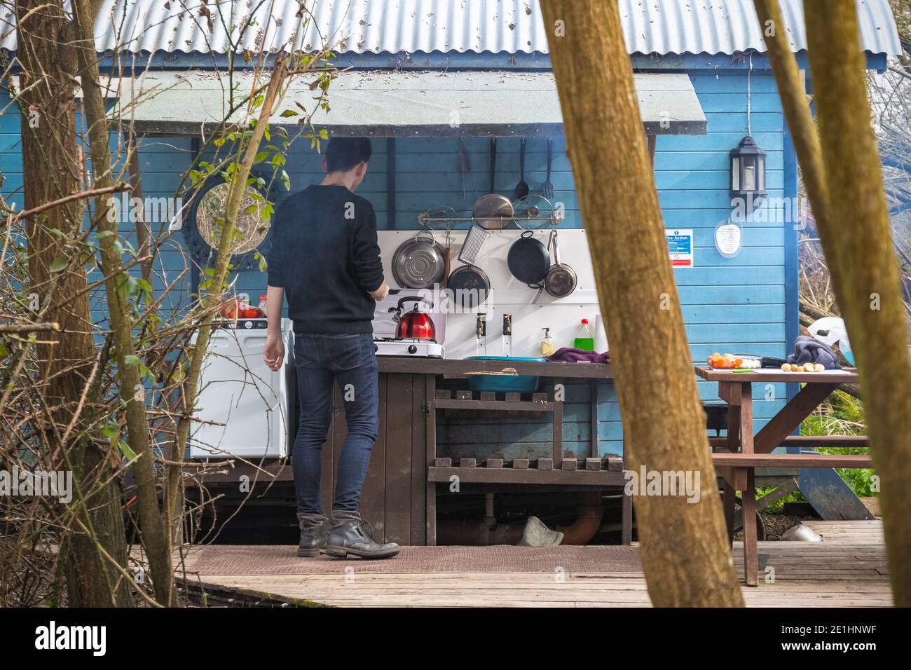 Man cooking with a basic facilities attached with converted train carriage at a camping site in Fairford, Gloucestershire, England Stock Photo