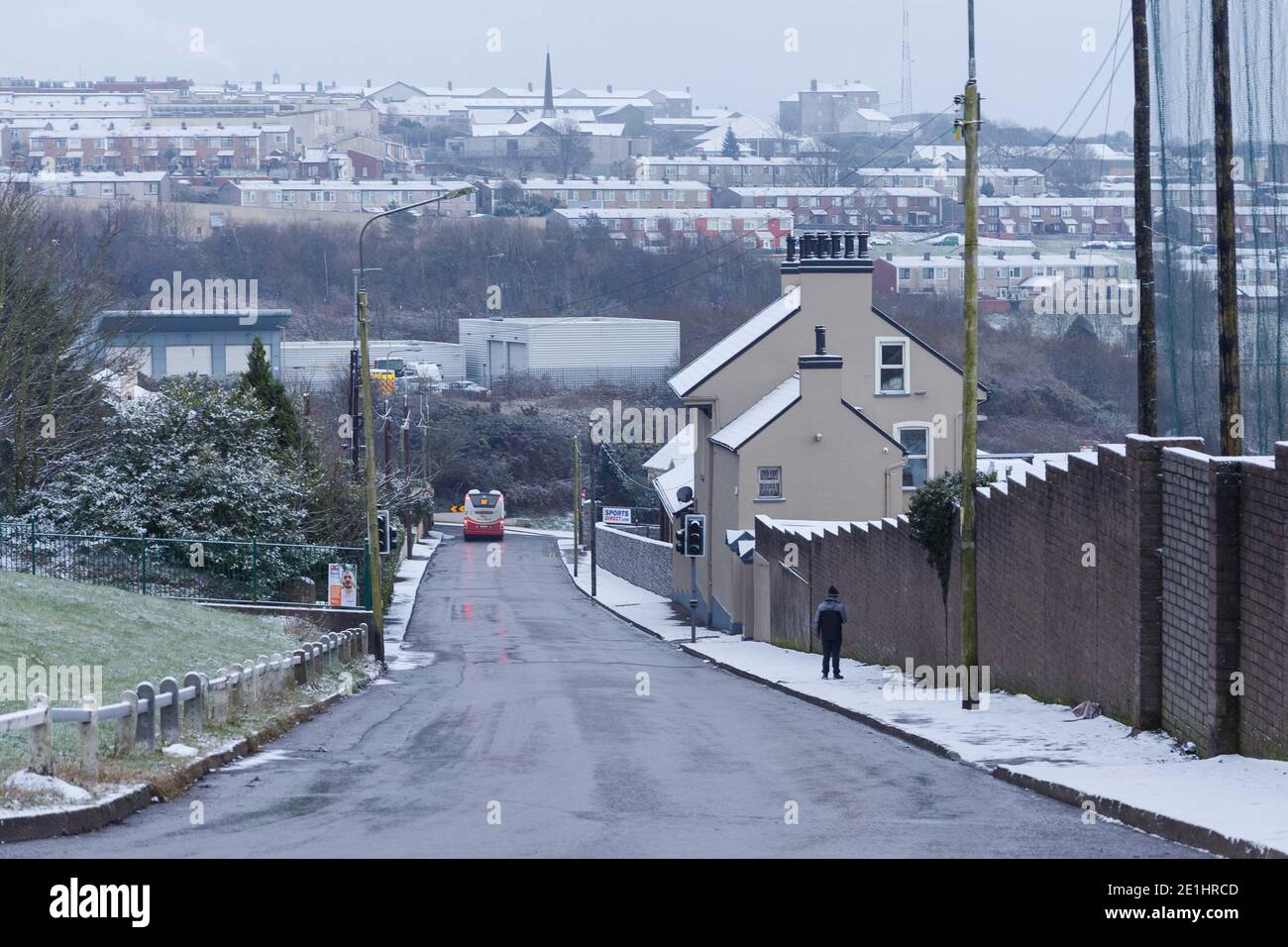 Cork, Ireland. 7th Jan, 2021. Snow Falls on Cork City. The 207 Bus making its way down Ballincollie Road folllowed by a pedestrian braving the paths. The people of Cork woke up this morning to the city and suburbs covered in a layer of snow following a short snow shower earlier this morning. Many wrapped up in coats and hats and went out to enjoy the crisp air and see the beautiful scenes. Credit: Damian Coleman/Alamy Live News Stock Photo