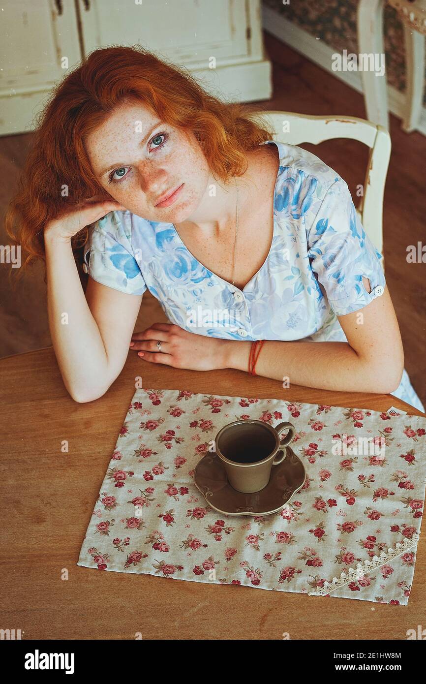 Portrait of young redhead woman  with freckles drinking coffee in sunny morning at home. Natural beauty. Woman's Day. Still life. Stock Photo