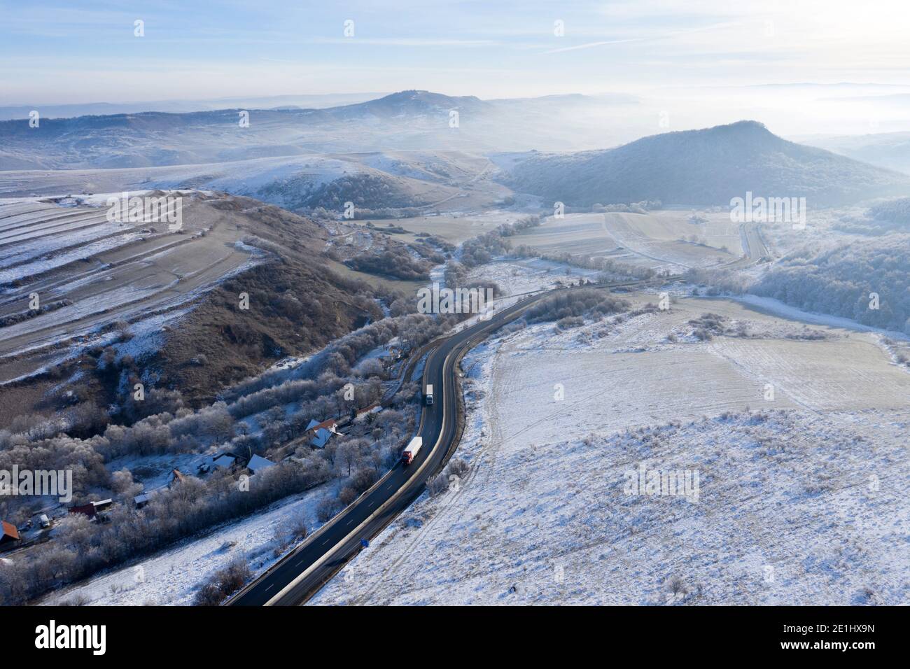 Aerial view of a winding road with trucks in a frozy winter sunny day ...
