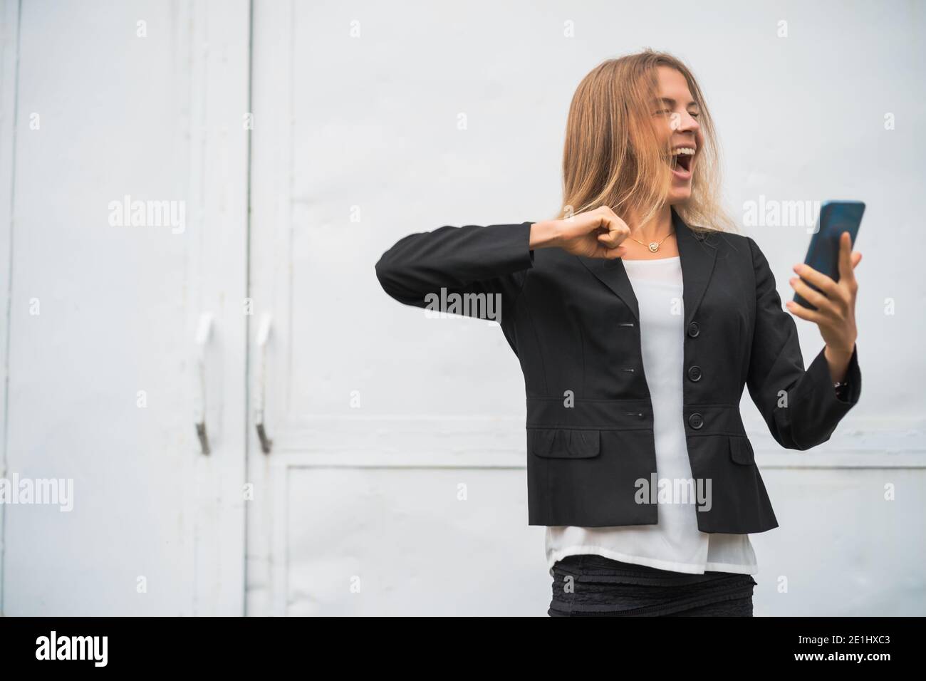 Outdoor portrait of ecstatic modern businesswoman who is joyful. She is holding smartphone. Stock Photo