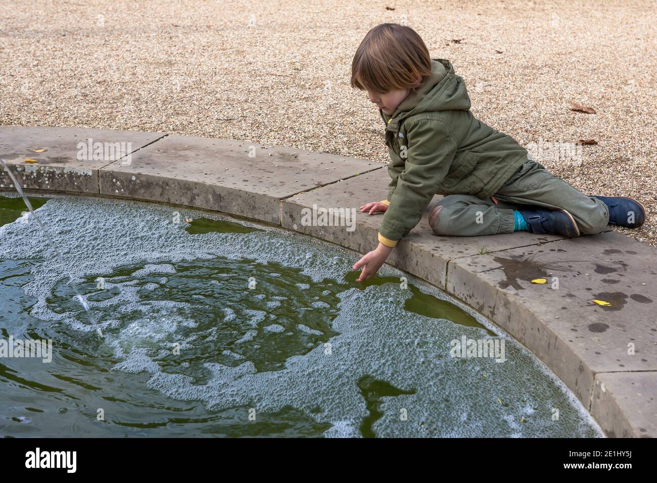 Little boy (3-4 years old) studies the pool of a fountain in the Collector Earl's Garden, Arundel Castle, West Sussex, England, UK.  MODEL RELEASED Stock Photo