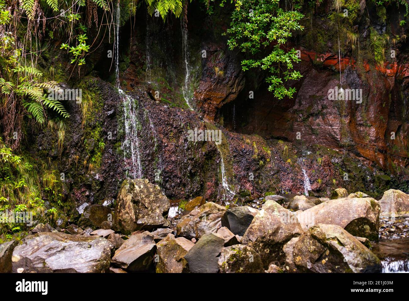 waterfall on madeira island on levada das 25 fontes tracking in wild nature with red rocks and stones Stock Photo