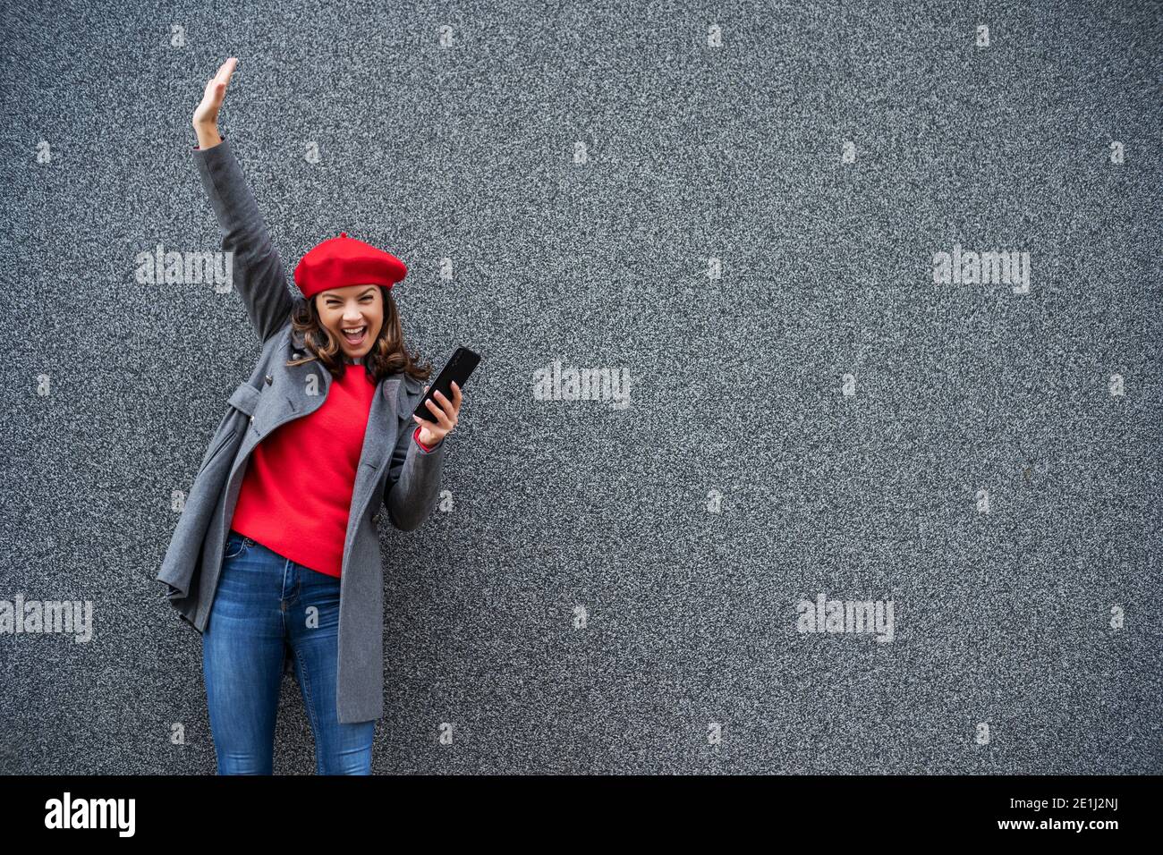 Adult woman in modern casual clothing standing in front of gray background. She is cheerful and looking at camera. Copy space for your advert. Stock Photo