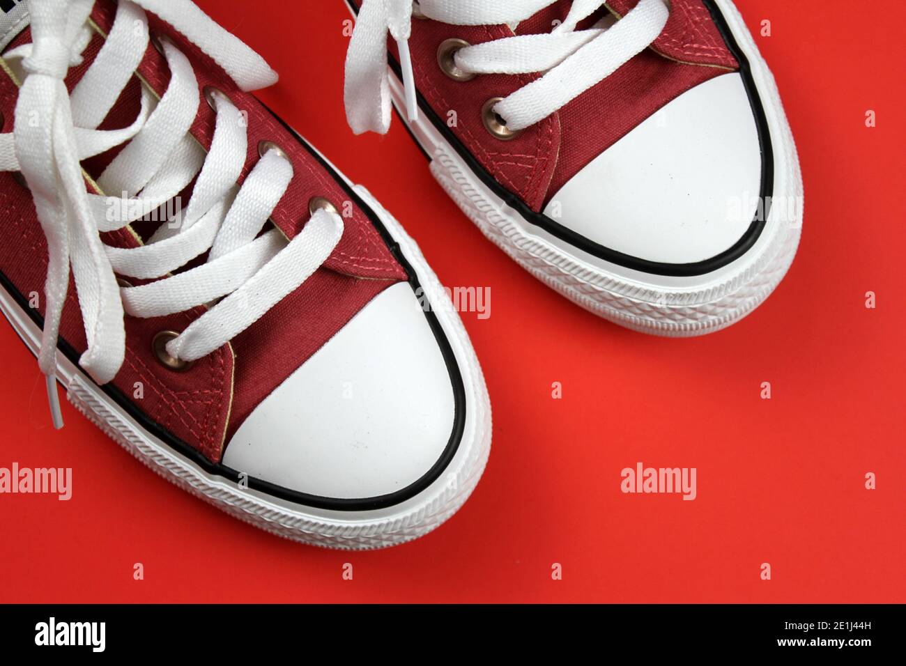 A pair of red pink sneakers with white laces against a stark red background. Stock Photo