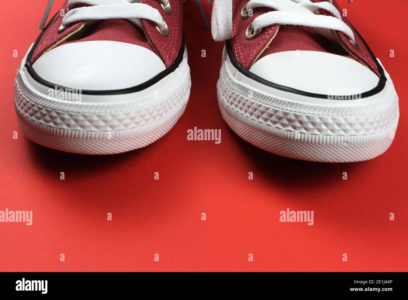 A pair of red pink sneakers with white laces against a stark red background. Stock Photo