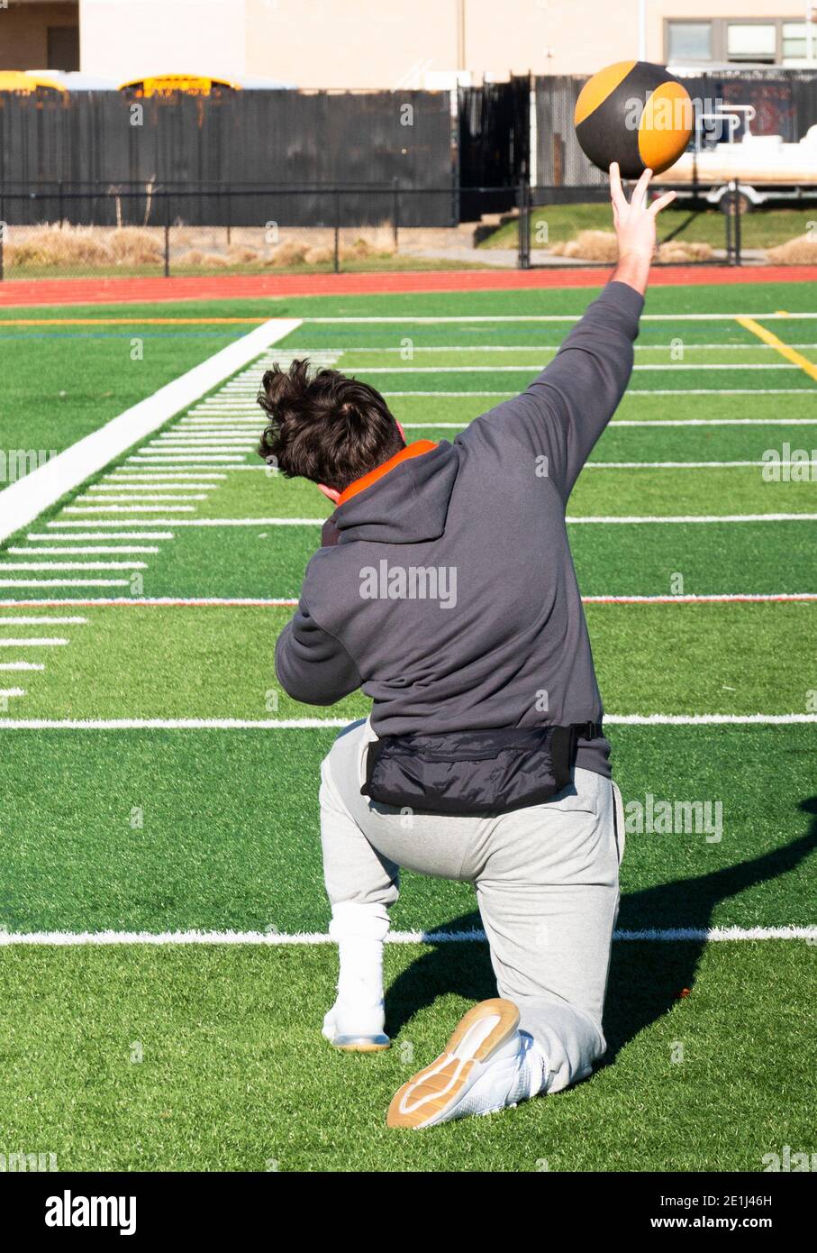 A high school athlete practicing for the shot put throwing event by throwing a medicine ball from his knees on a green turf field at track and field p Stock Photo