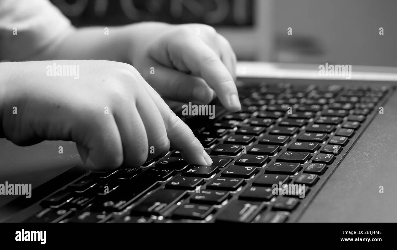 Black and white closeup photo of child pressig buttons on computer keyboard, typing message on laptop keyboard. Stock Photo