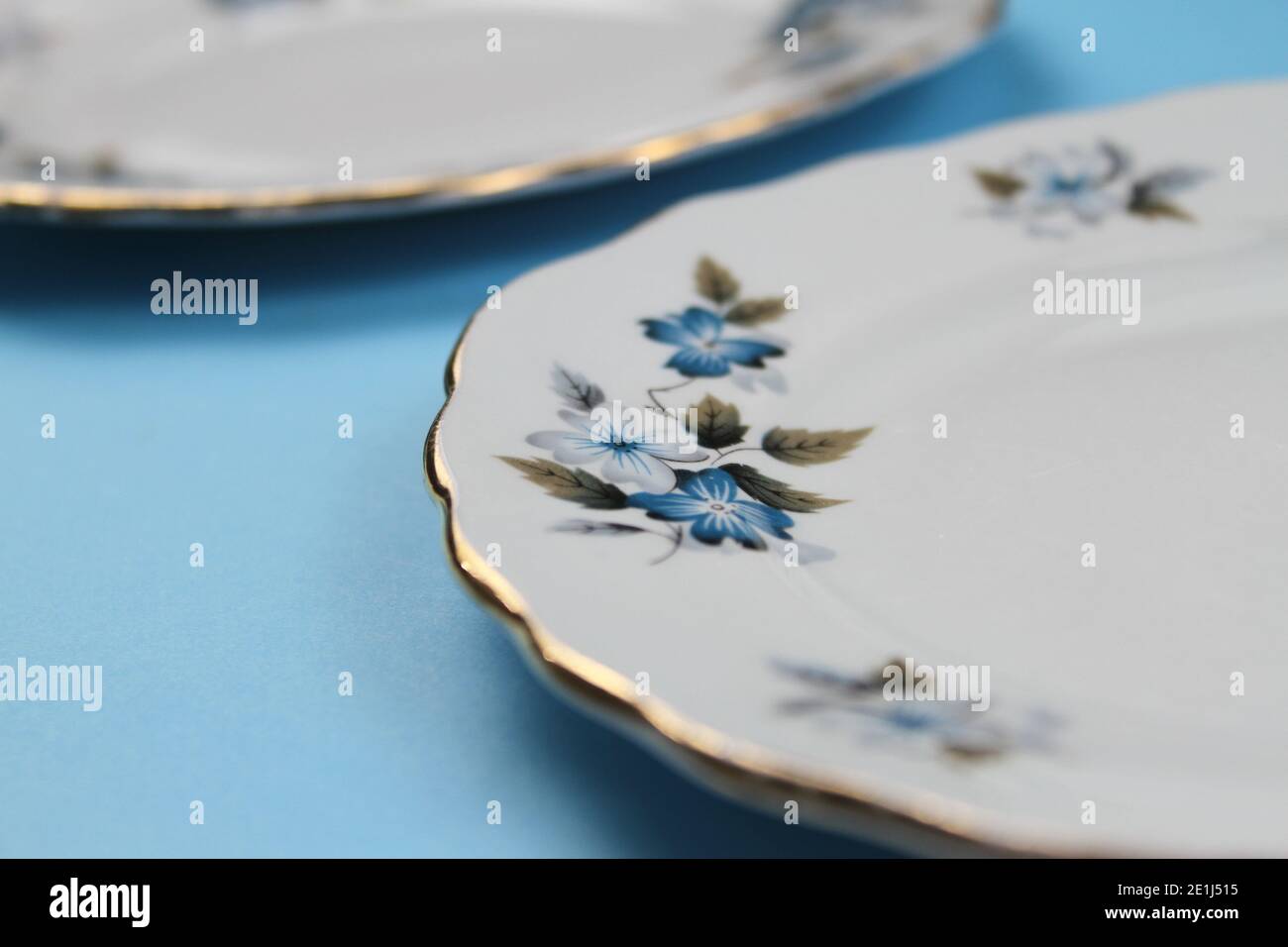 Close-up of a vintage gold-rimmed plate with blue flower detail against a plain background Stock Photo