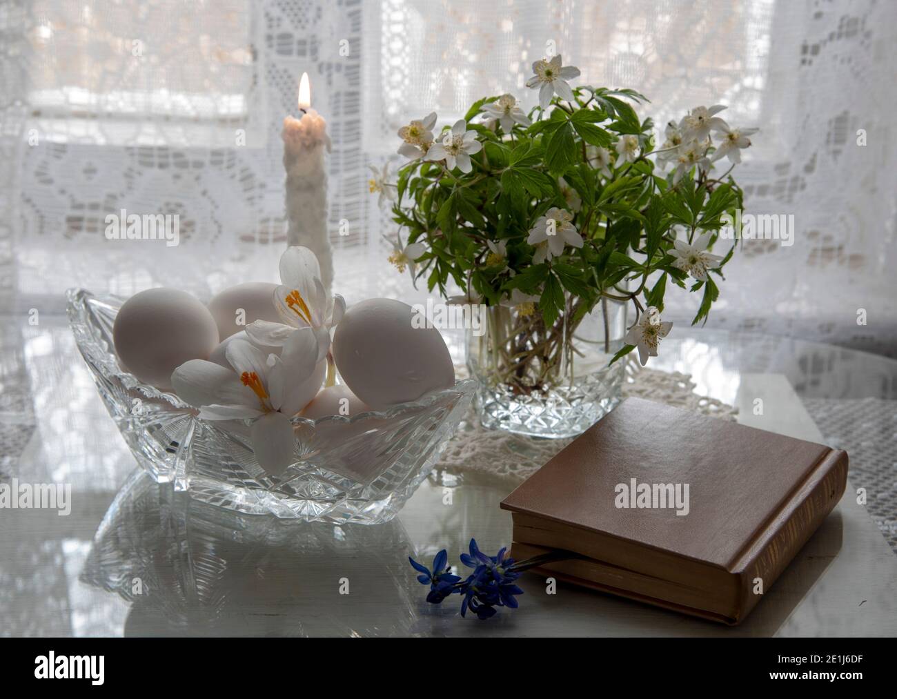 Spring flowers in a glass and white eggs in a crystal vase on a white background. Stock Photo