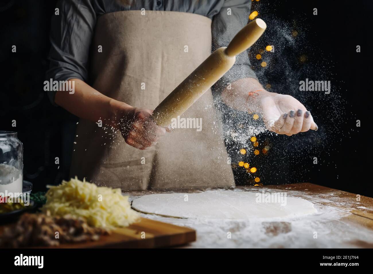 Home Made Pizza Cooking. Woman hands keep rolling pin with flour on dark brown table. Food preparing concept under quarantine due to epidemic. Stock Photo