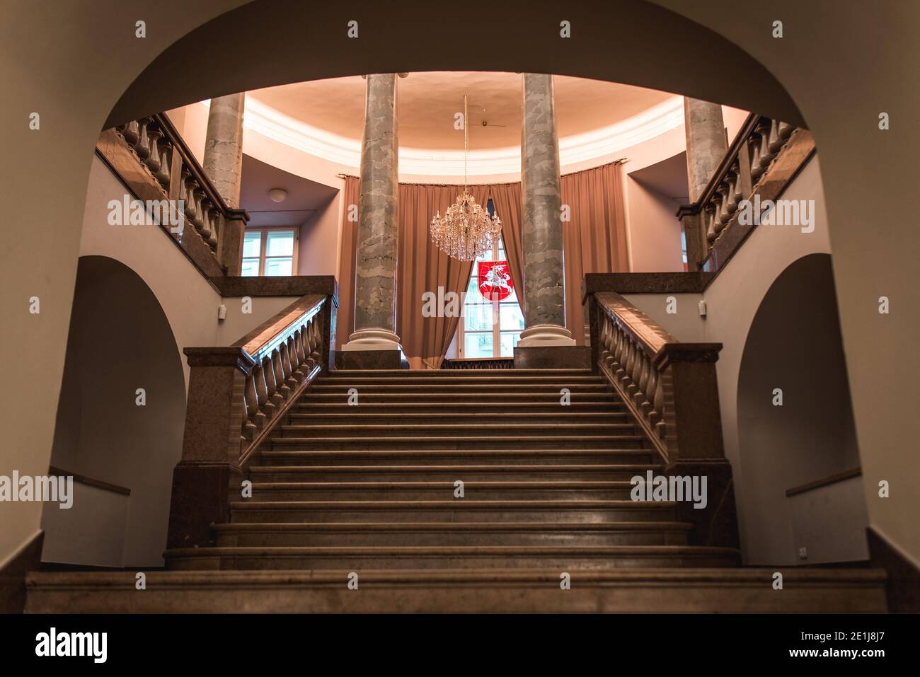 Vilnius, Lithuania - November 9, 2019: Interior of the Town Hall. Staircase leading to the columns, and window with curtains, coat of arms in middle. Stock Photo