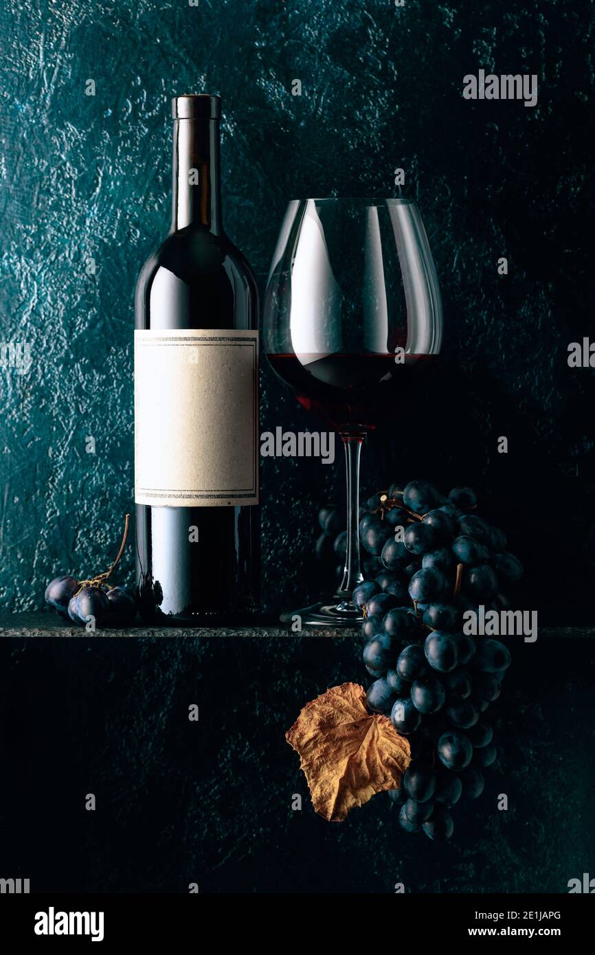 Red wine and blue grapes with dried up vine leaves on an old dark blue ...