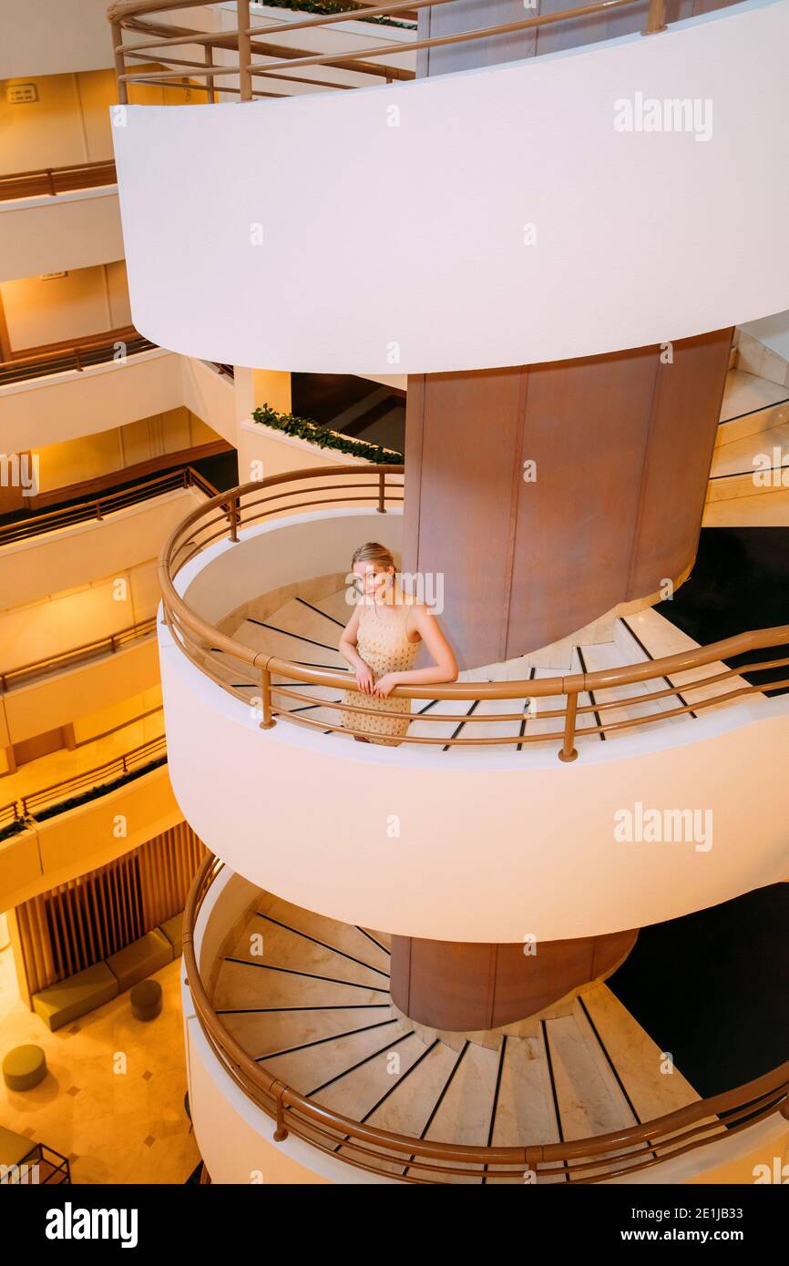Pretty blonde girl standing on spiral stairs, holding the railing Stock Photo