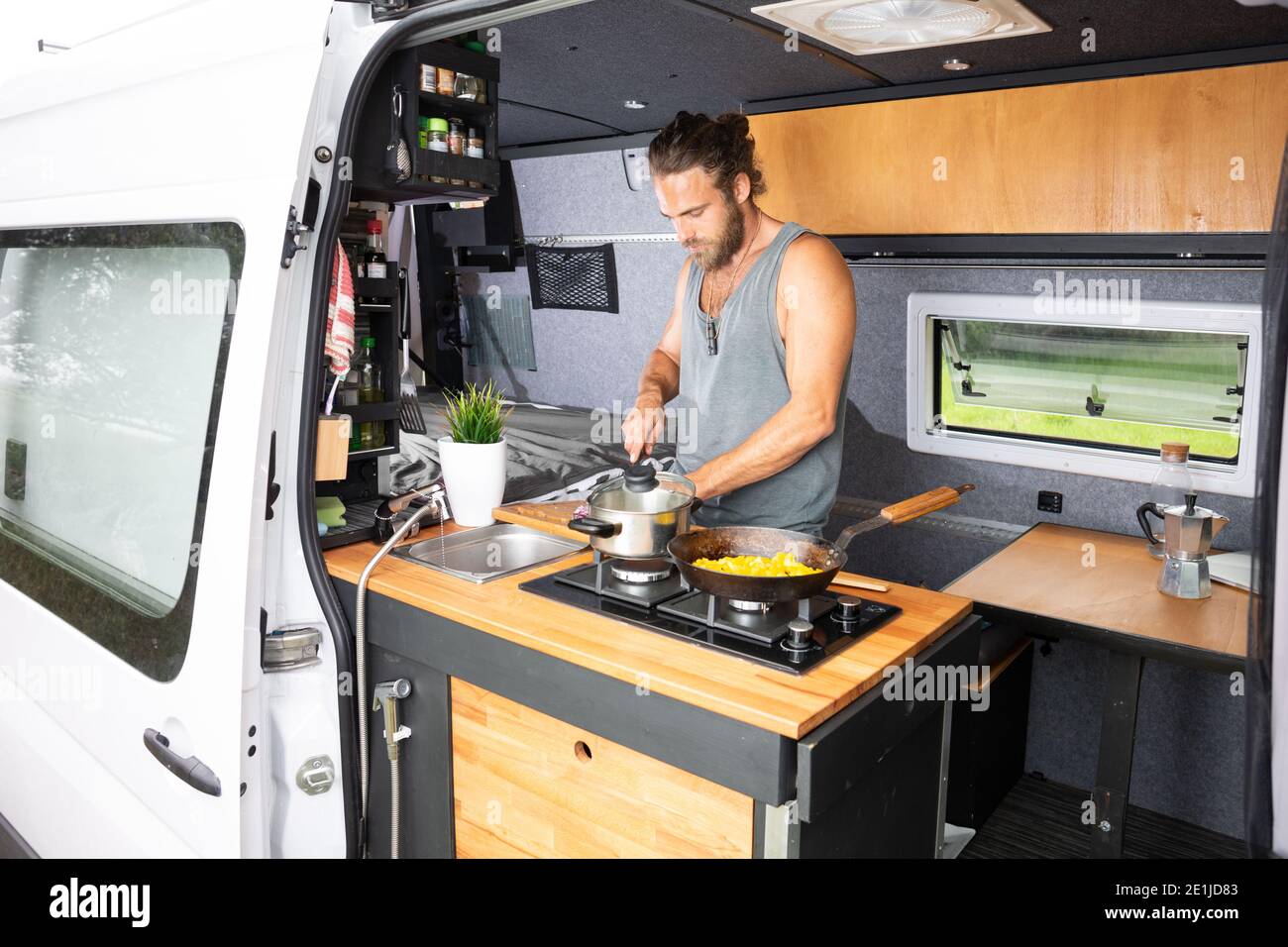 Man cooking in the kitchen area of his camper van Stock Photo