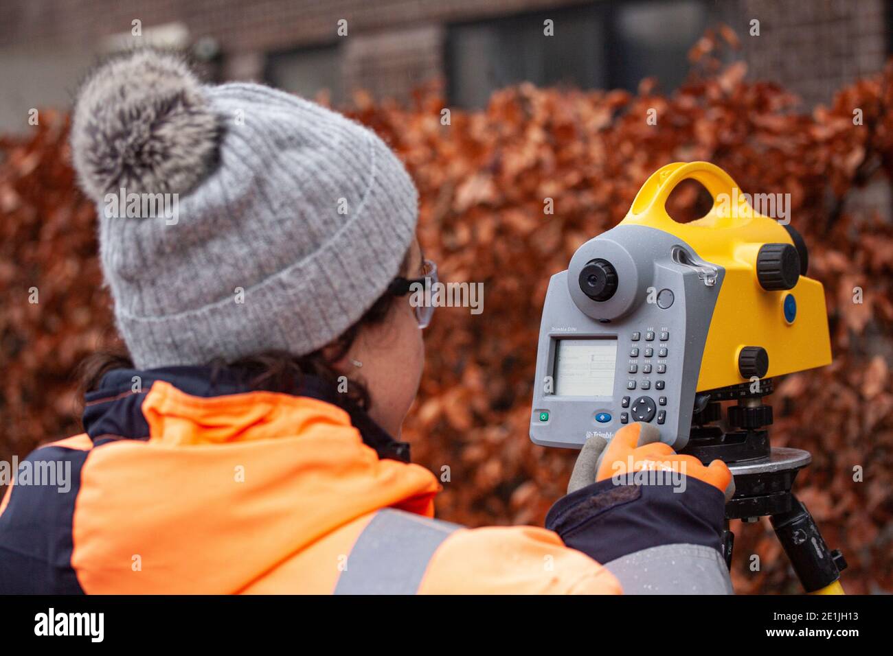 Female land surveyor operating a digital precision measurement level to establish or verify or measure the height of specified points relative to a da Stock Photo