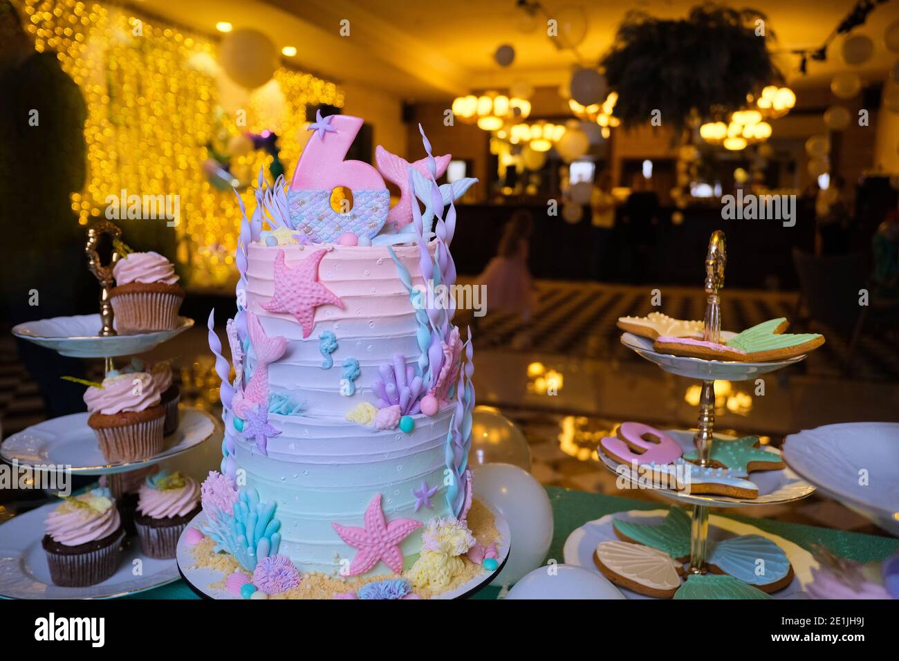 Delectable birthday Mermaid theme cake decorated with colorful seashells and starfish with number 6 served on table with cupcakes and sweets during ce Stock Photo