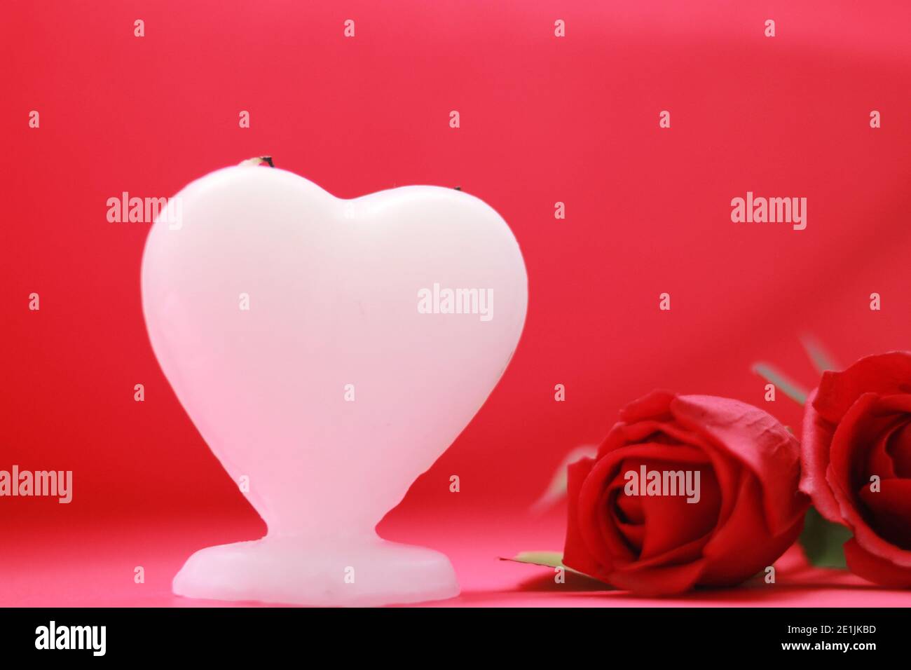 white heart shaped candle with two roses, red background, for love and ...