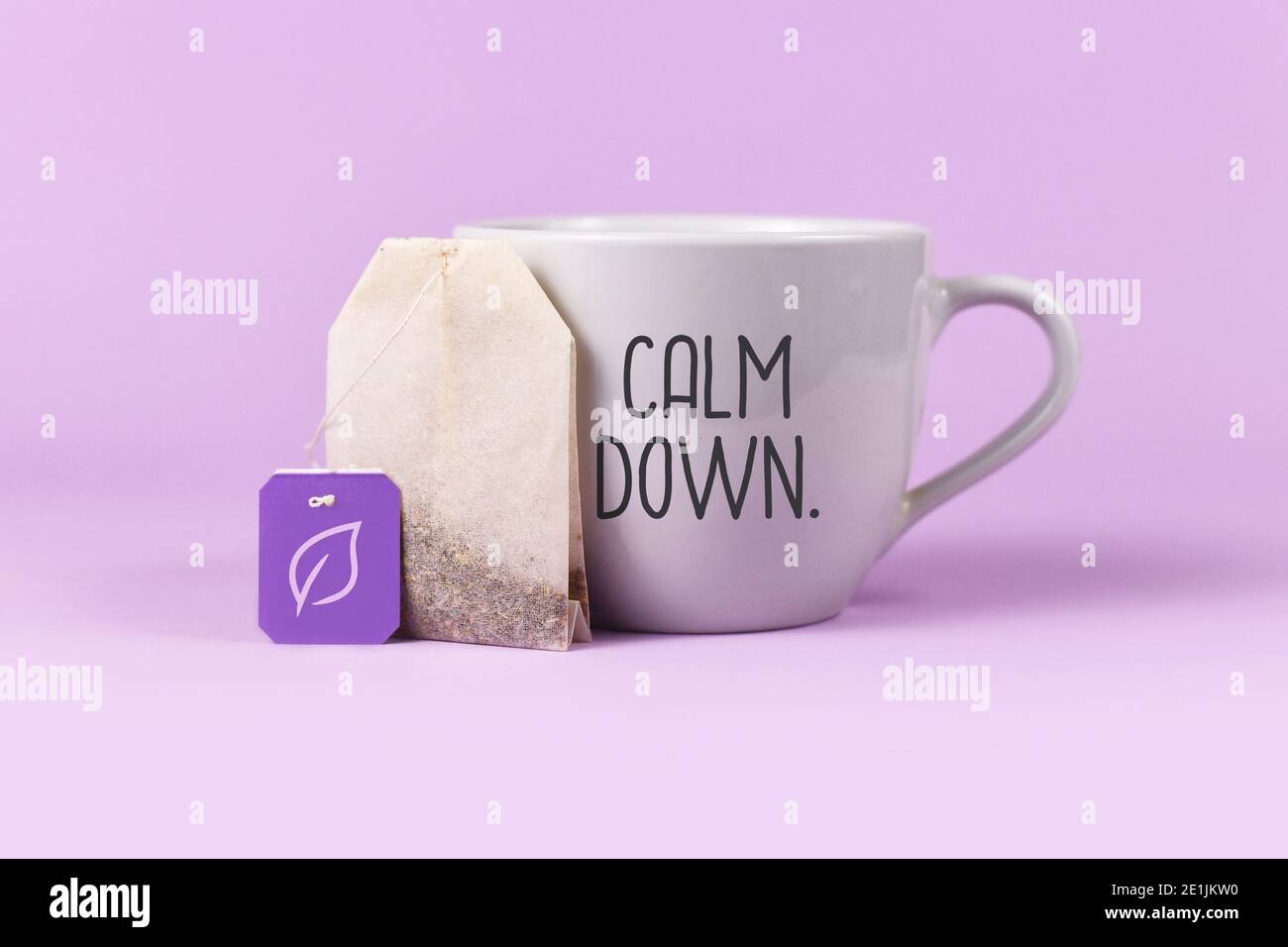 Concept for calming herbal tea with tea bag with leaf on labelnext to tea cup with text 'Calm down' on violet background Stock Photo