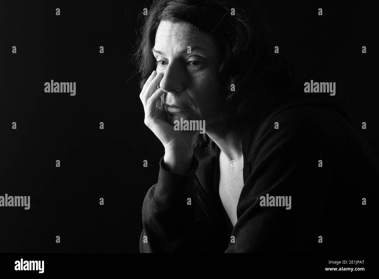 pensive woman with downcast eyes on black background Stock Photo