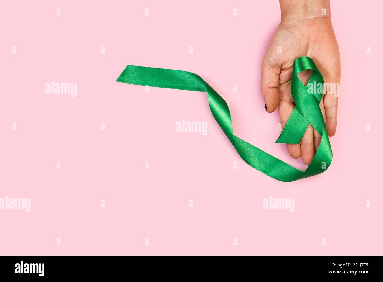 Woman hand holding a green ribbon on a pink background Stock Photo