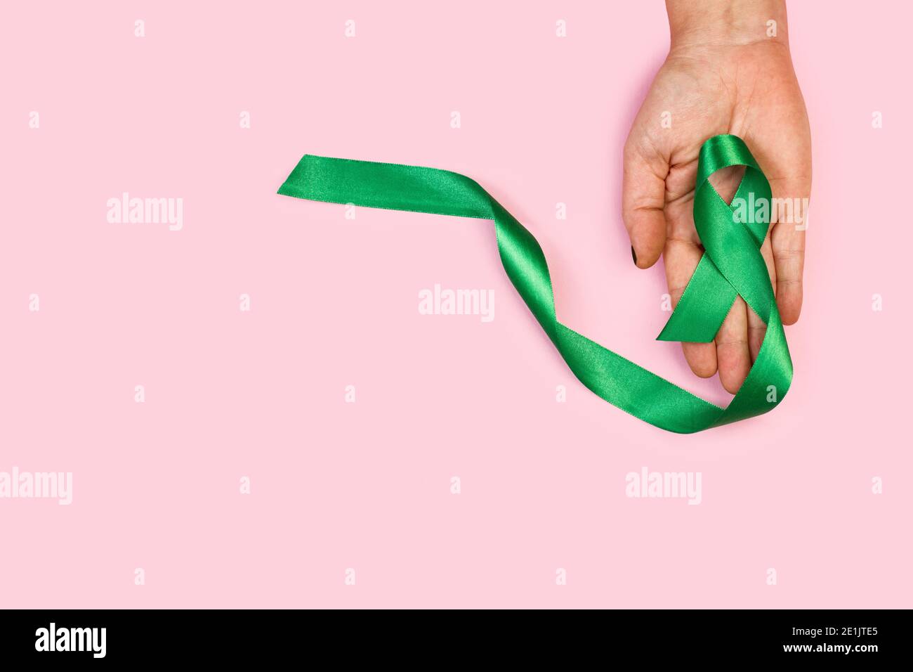 Woman hand holding a green ribbon on a pink background Stock Photo - Alamy