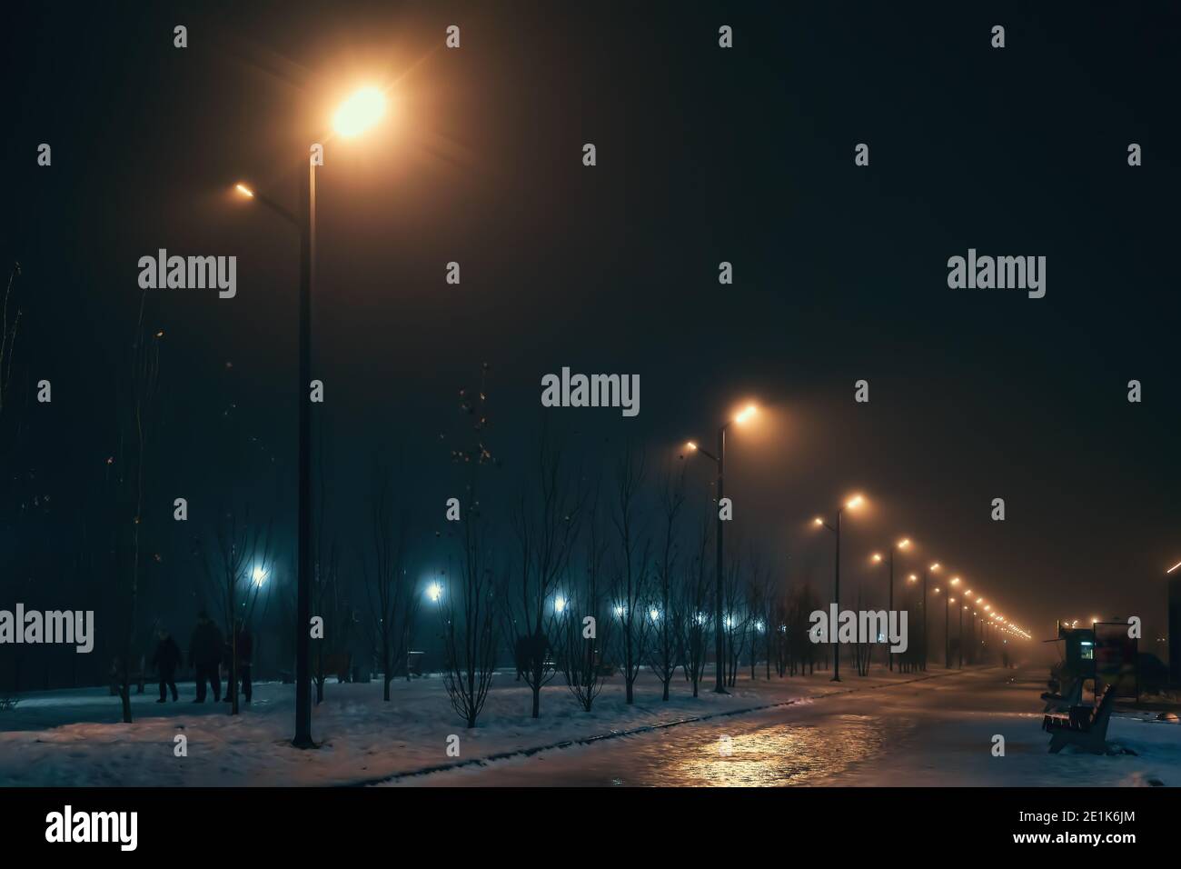 Urban alley in foggy winter night illuminated by street lamps. Stock Photo
