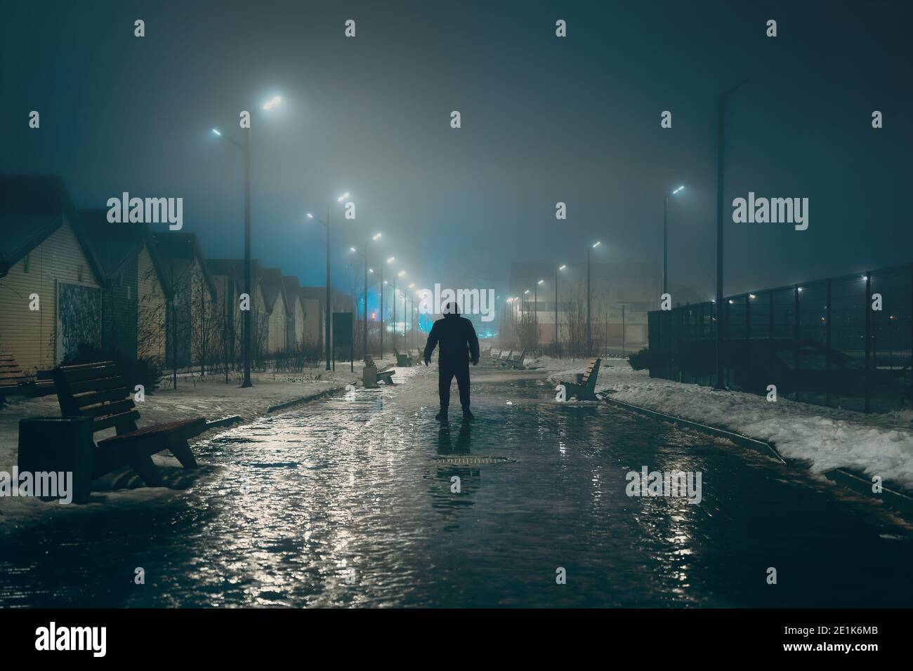 Silhouette of dark man in hood in night illuminated city alley in foggy weather, misty horror and scary atmosphere concept. Stock Photo