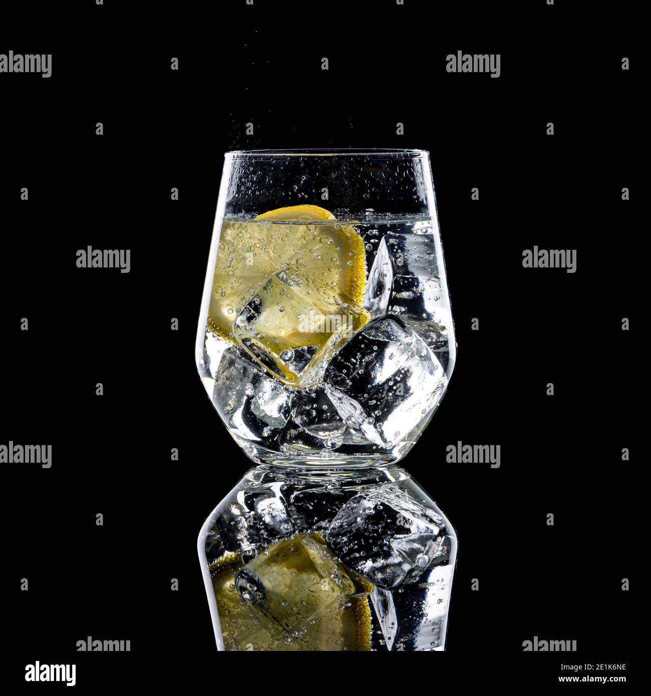 Gin and Tonic with ice cubes and slice of lemon in glass on black background Stock Photo