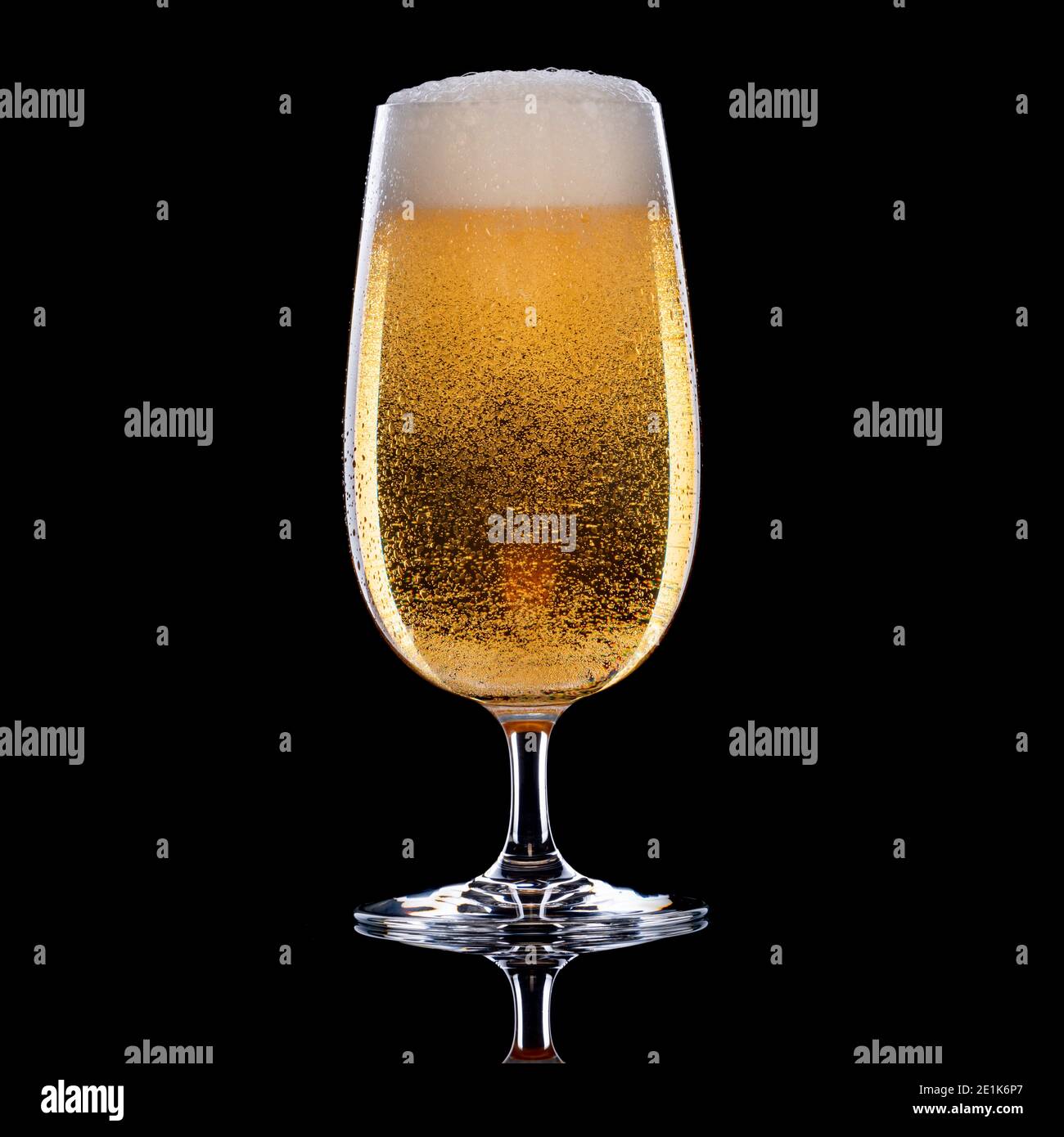 Beer with foamy head in tall stemmed glass on black background Stock Photo