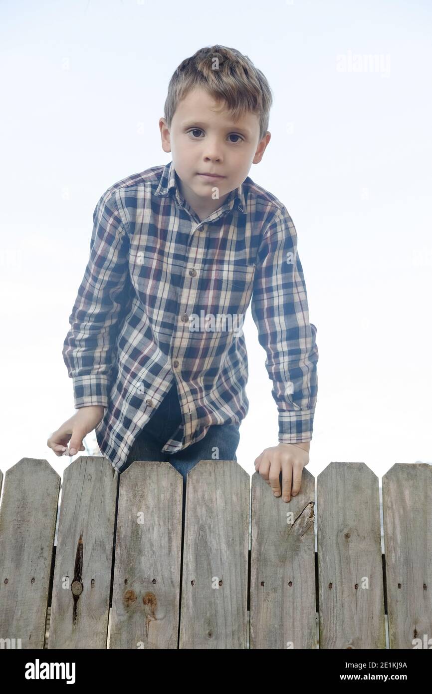 Cute country boy in checkered shirt sits on a fence. Concept child activity  Stock Photo - Alamy