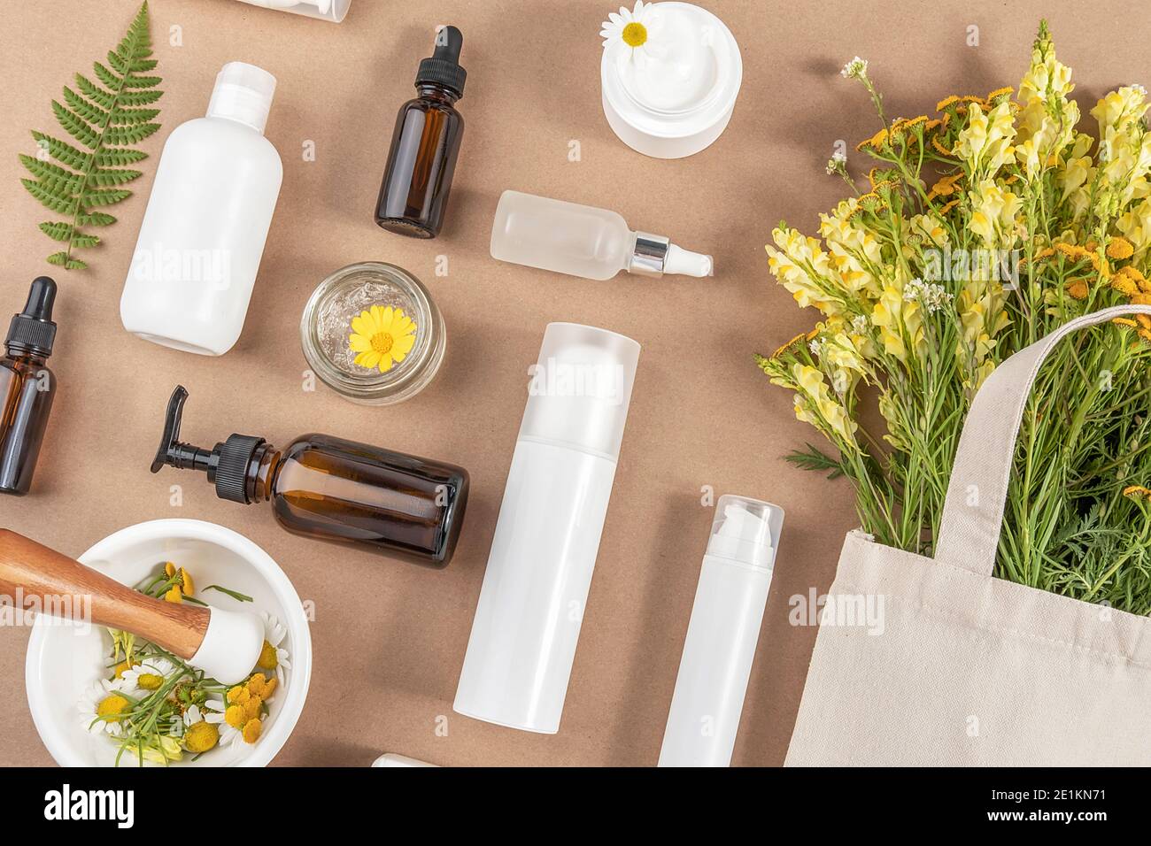 Various bottles, tubes, jar with cosmetic, wildflowers in eco textile bag, mortar bowl with pestle on beige background. Concept natural herbal organic Stock Photo