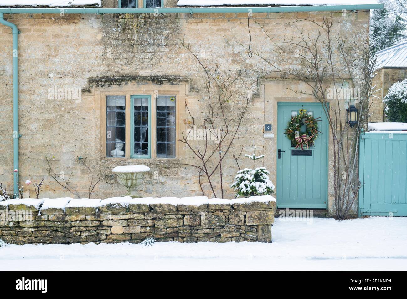 Cotswold stone cottage with christmas wreath in the December snow