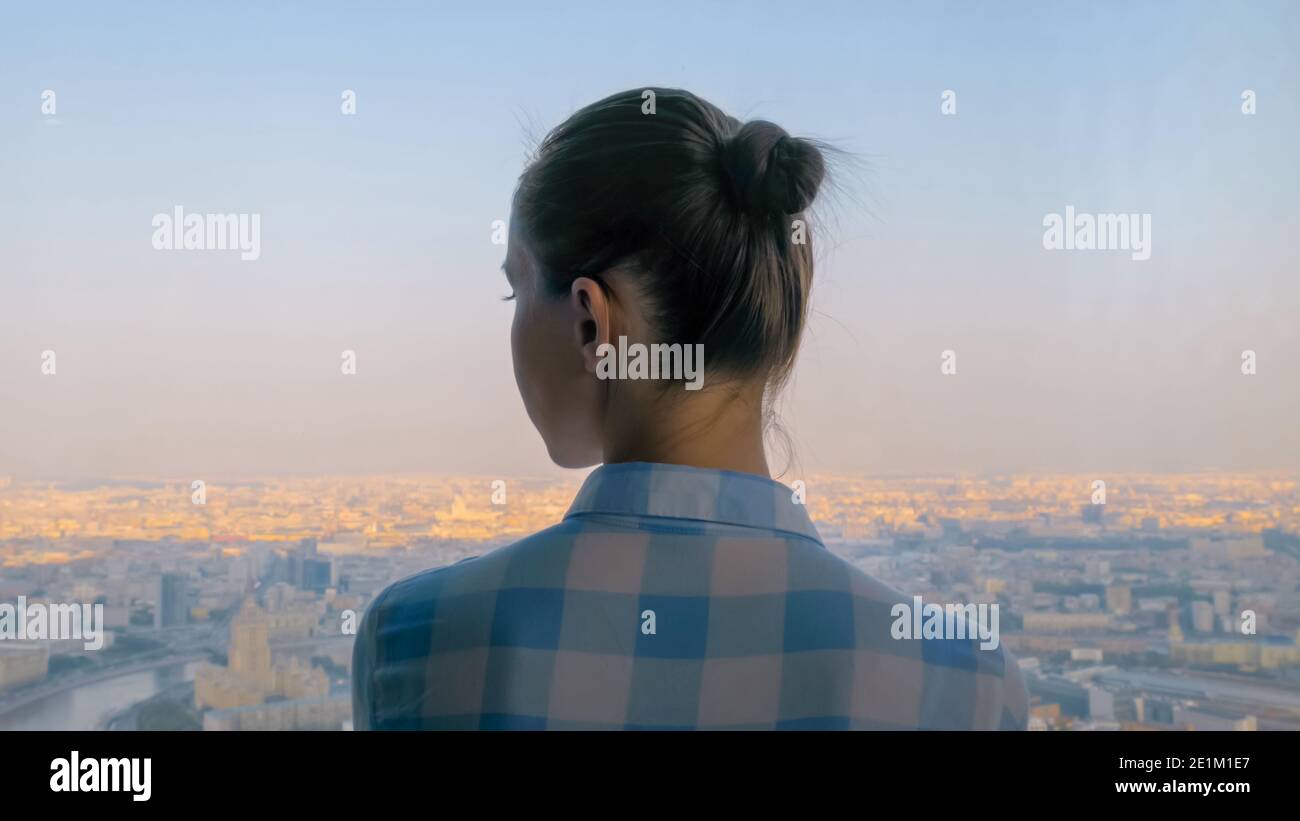 Back view of pensive woman looking at cityscape through window of ...