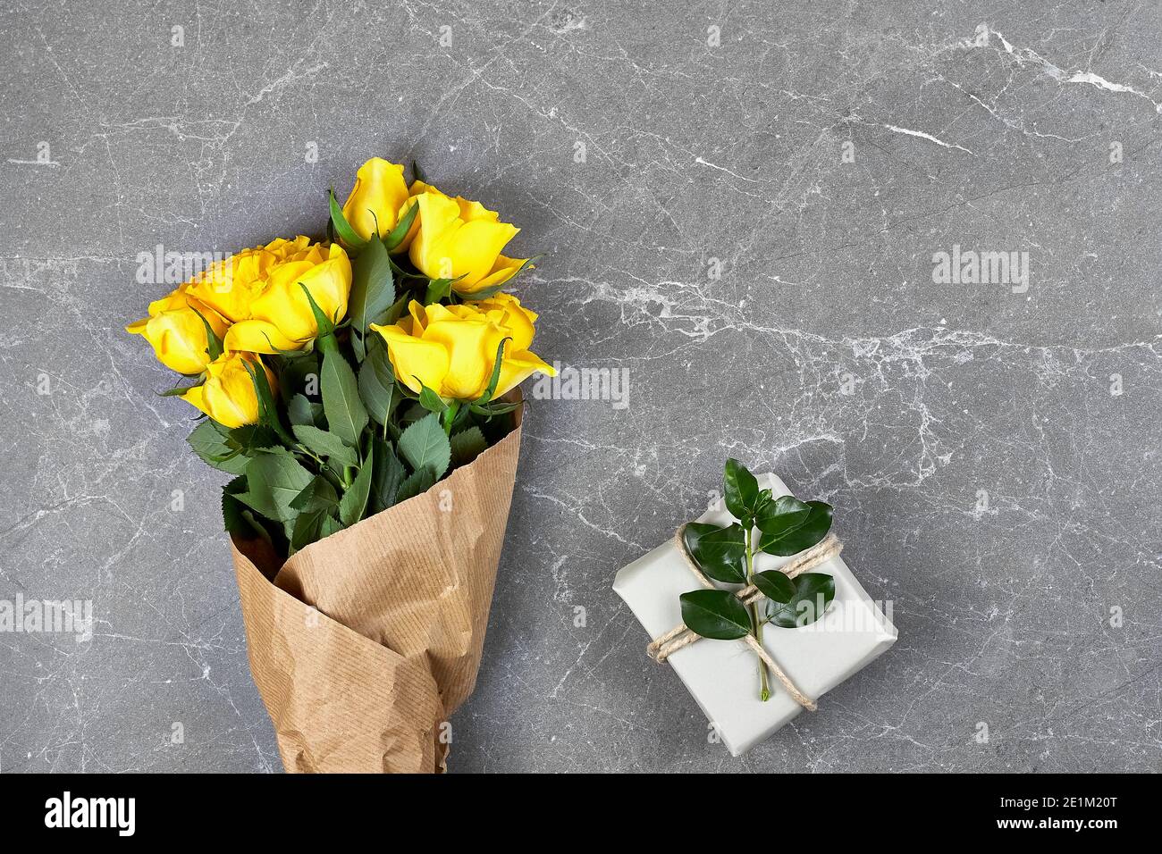 Yellow roses in craft paper and trendy gift box in recycled paper on gray background. Natural aestetic. Valentines day,Mothers day,Womens day flat lay Stock Photo