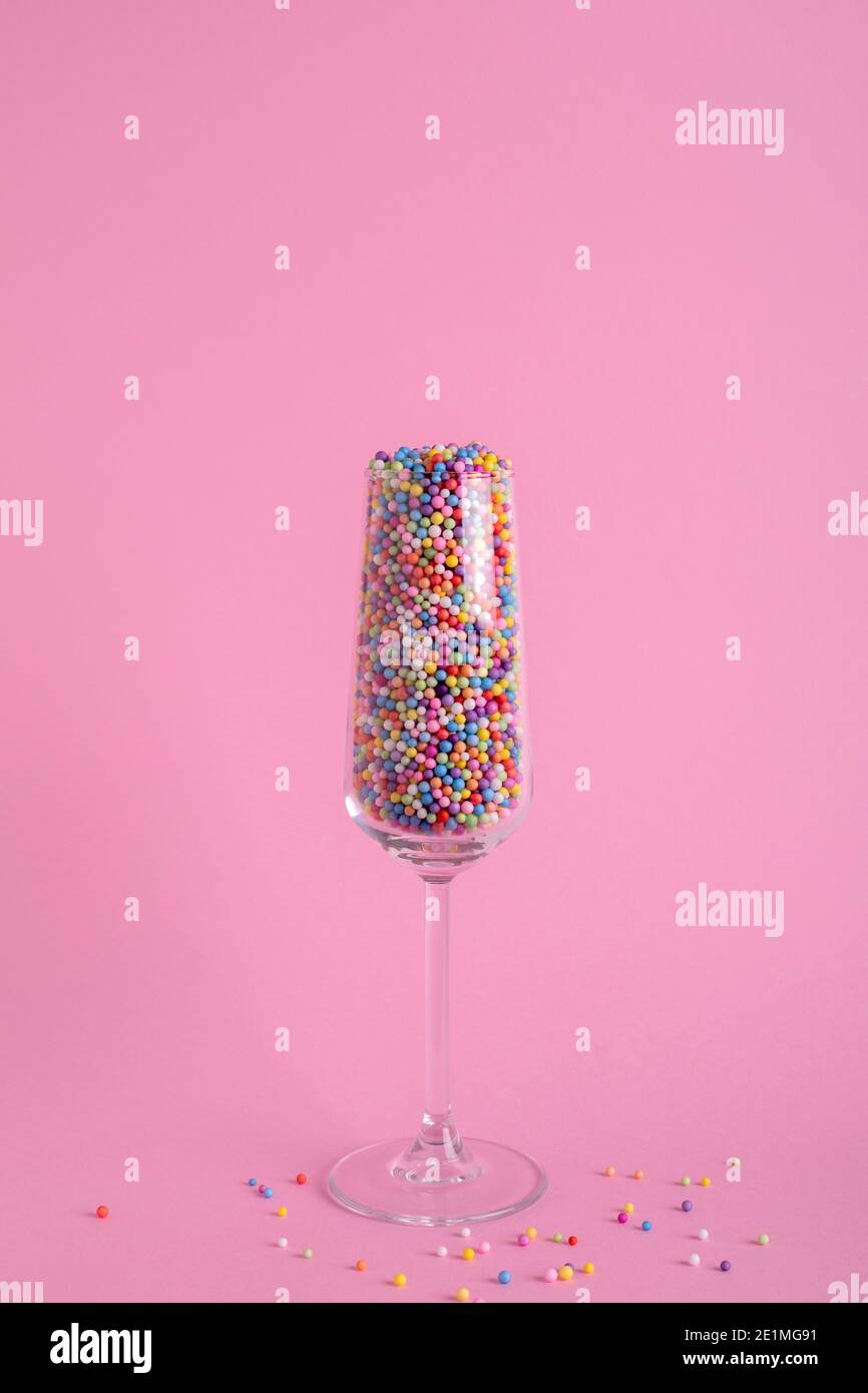 Champagne glass filled with colorful balls on pink background, party concept Stock Photo