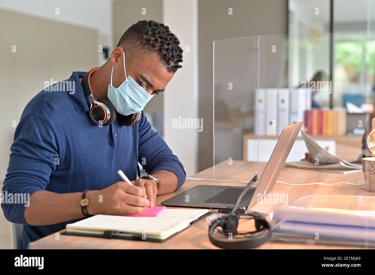 Office-worker in open-space office protected by plexiglas, wearing surgical face mask Stock Photo