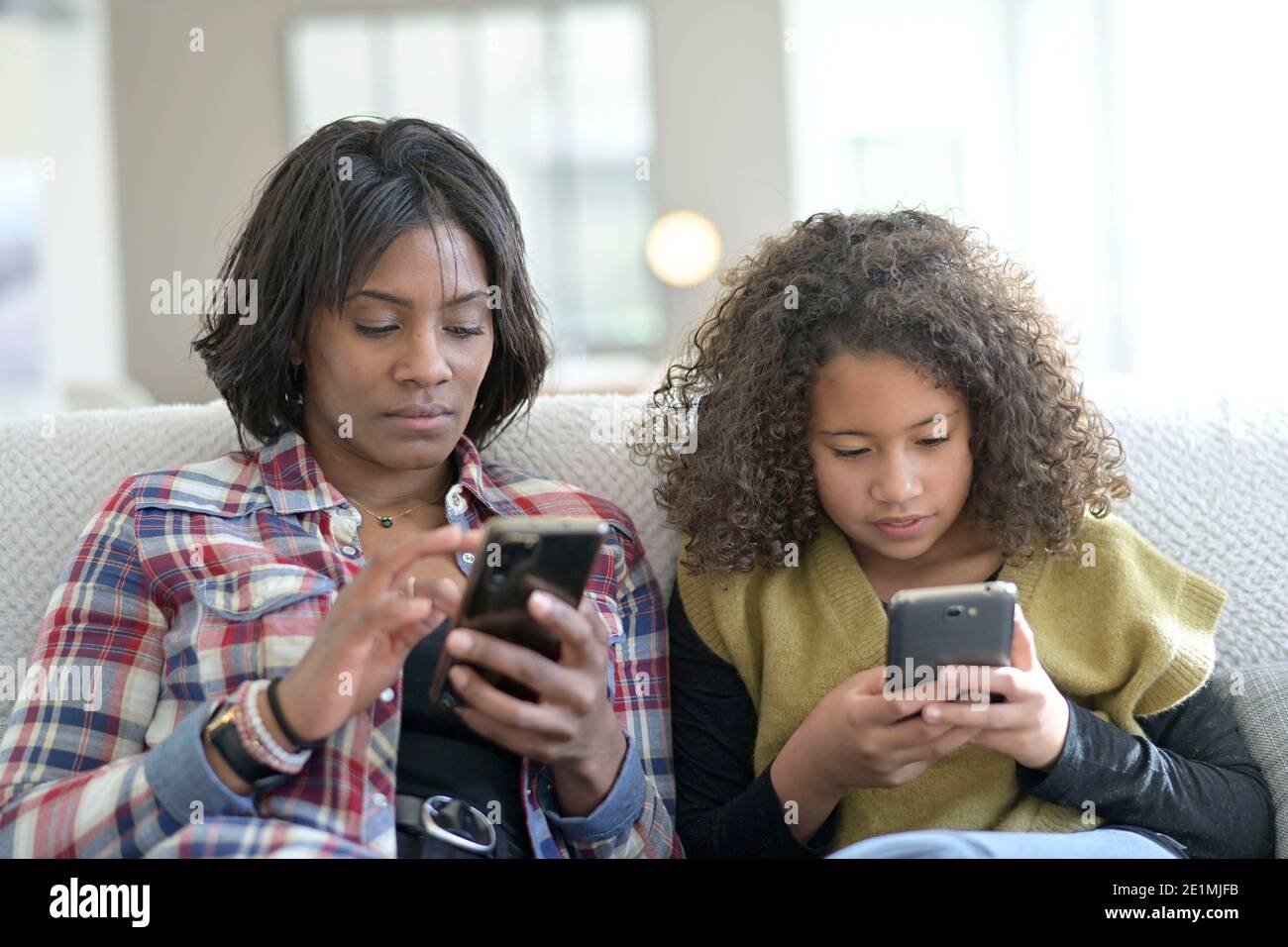 Mother and daughter chilling in sofa and using smartphone Stock Photo