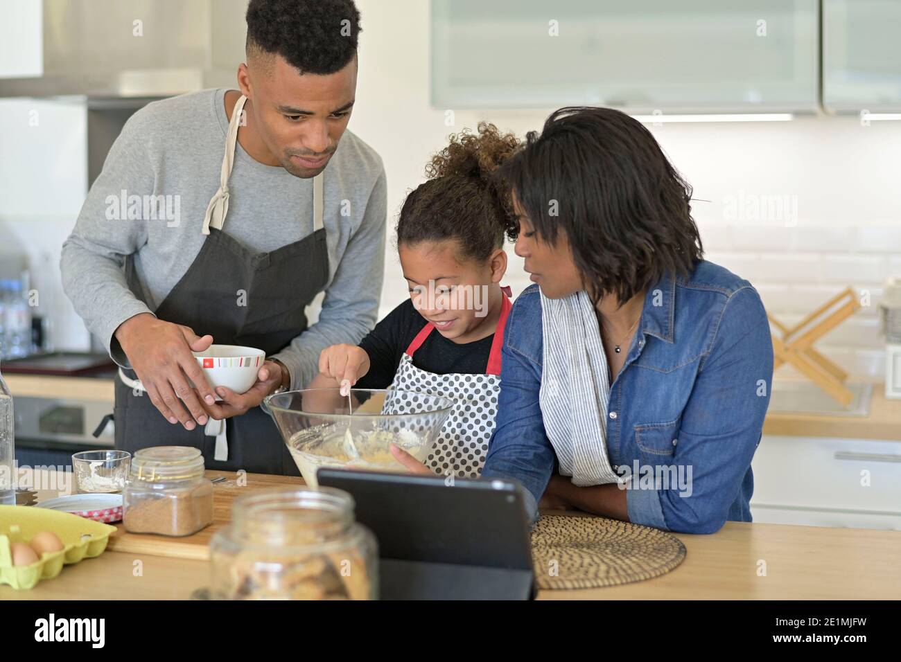 Happy family in home kitchen making american cookies looking at recipe online Stock Photo