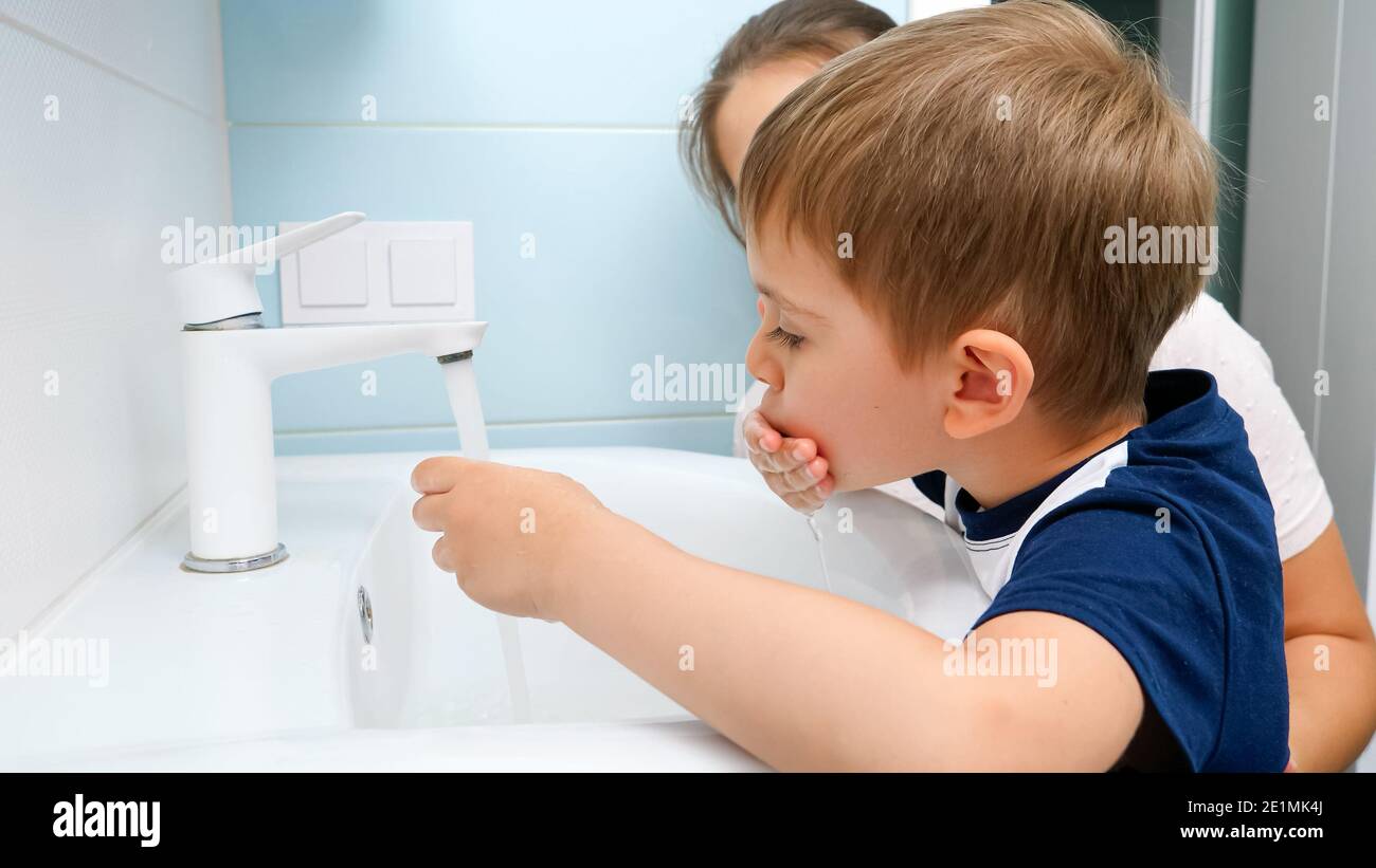 Portrait of smiling little boy with mother washing and cleaning dirty mouth with water in the