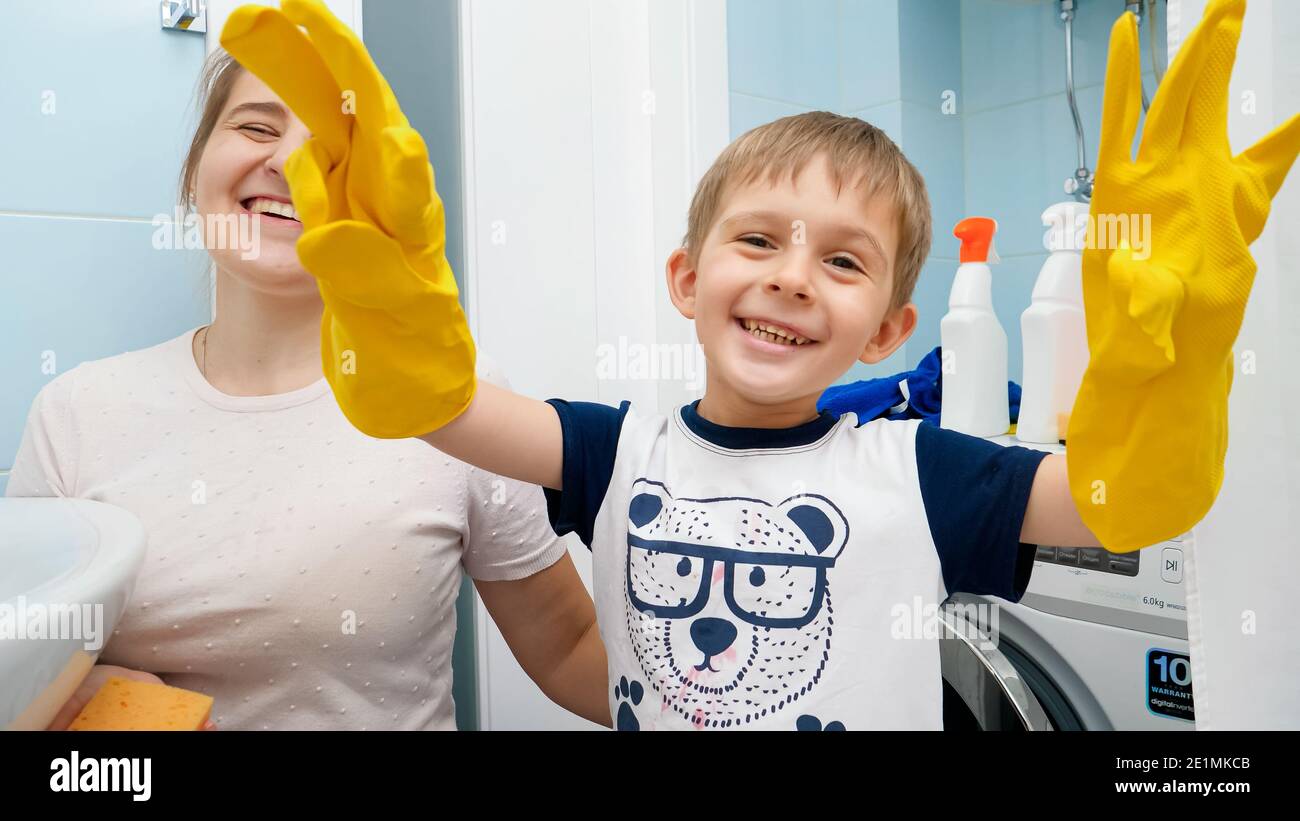 Happy smiling little boy in yellow rubber gloves doing housework and